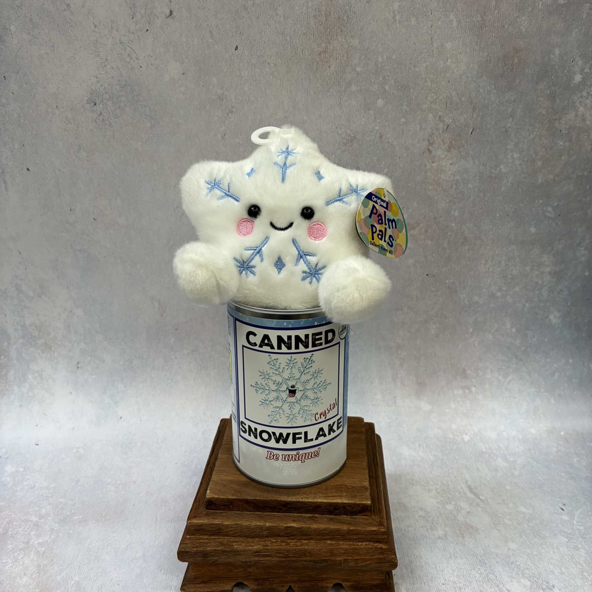 Plush snowflake toy sitting on a canned container on a wooden stand