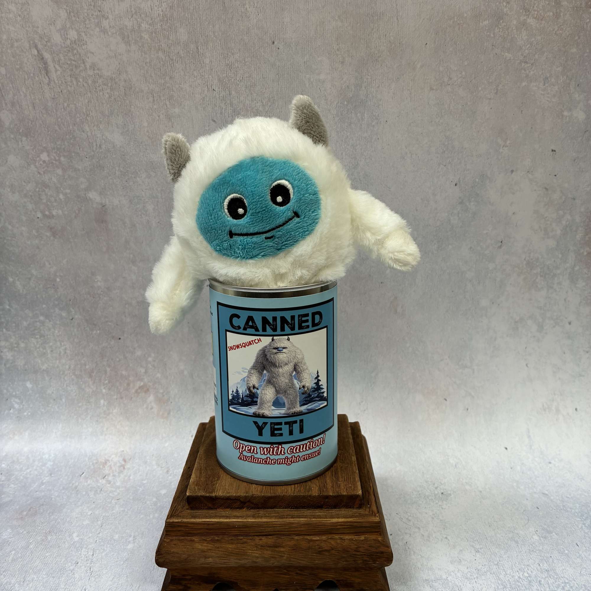 Plush yeti toy sitting in a labeled can on a wooden stand
