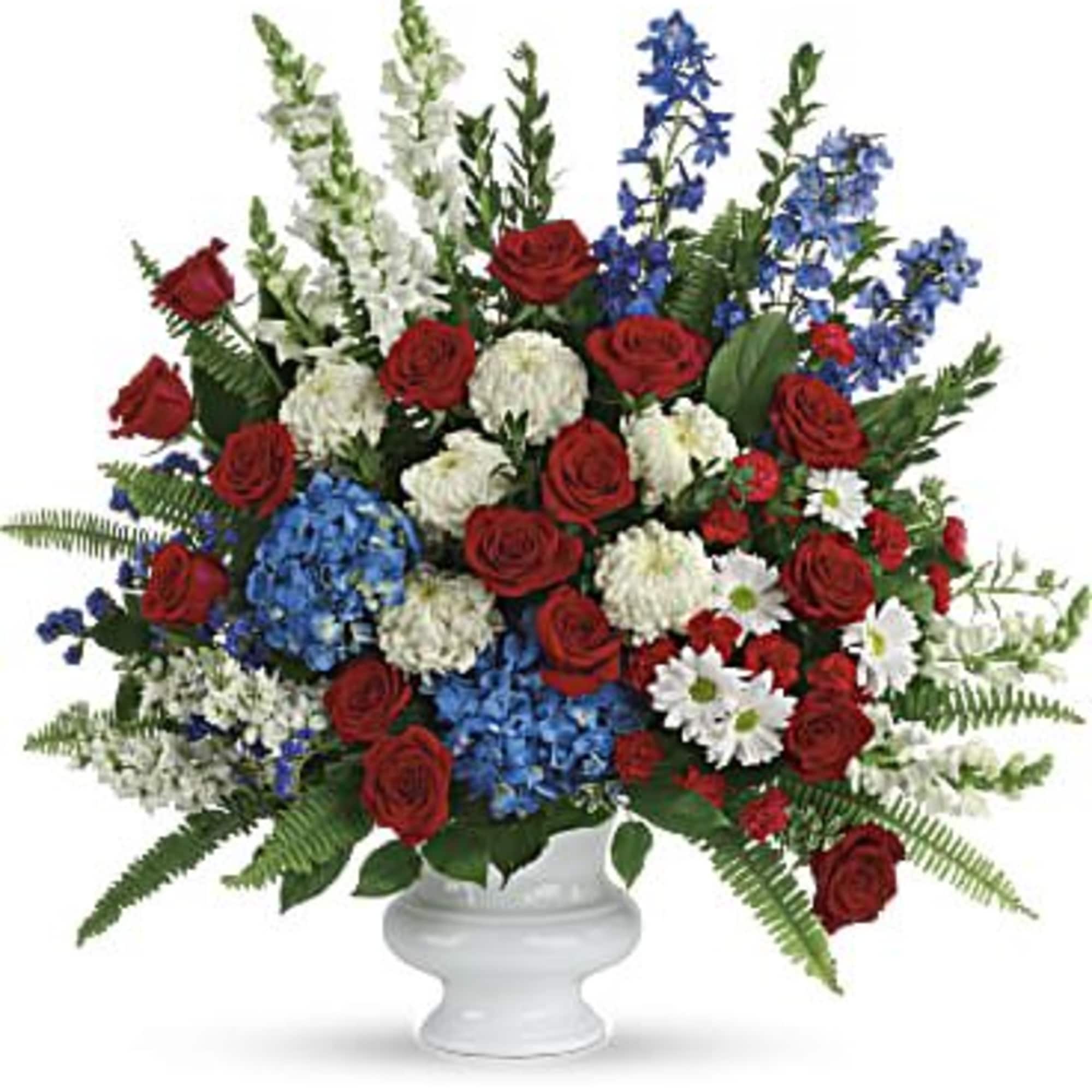 Large red, white, and blue arrangement with roses and mixed flowers in a white pedestal urn