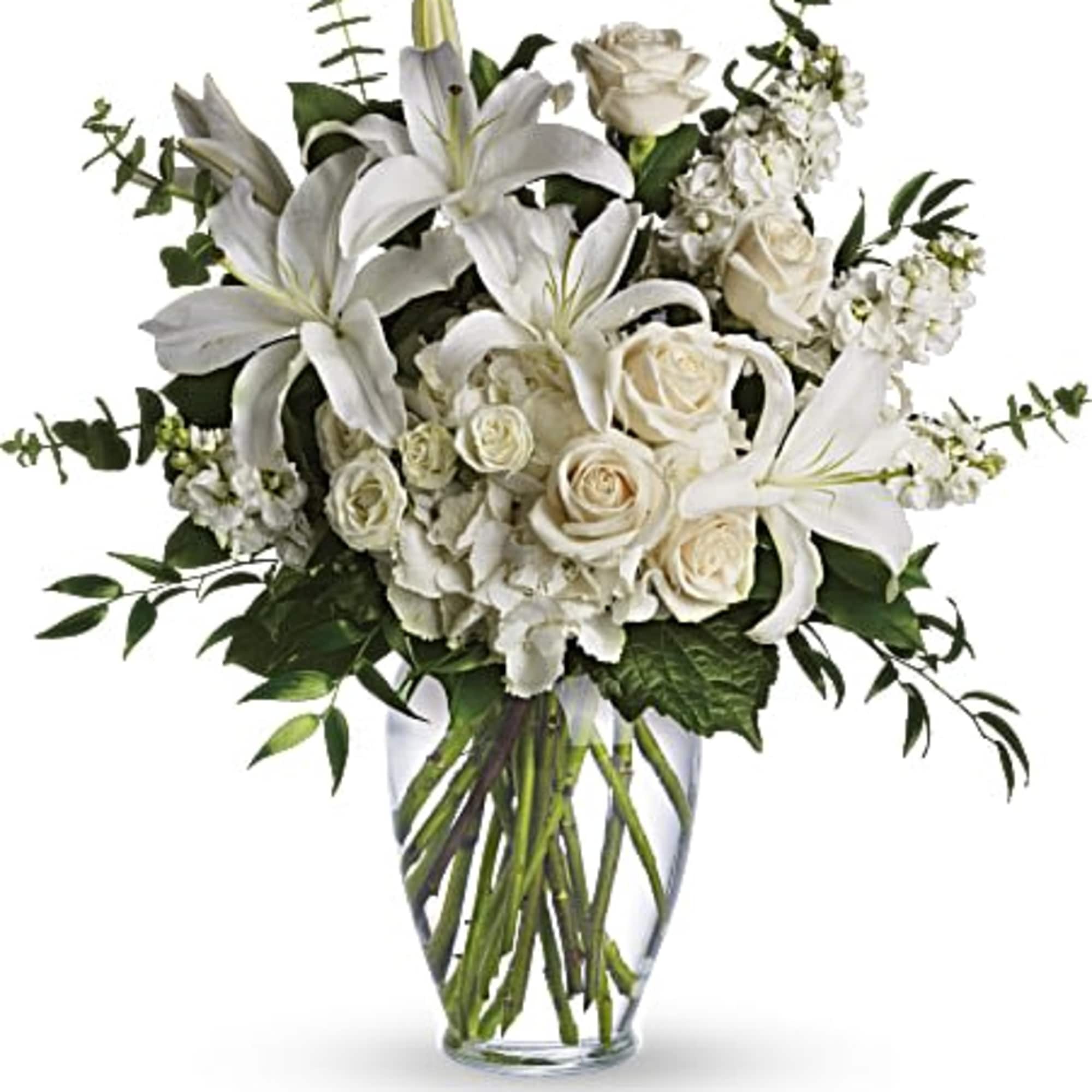 Tall arrangement of white lilies, roses, and other white flowers in a clear glass vase