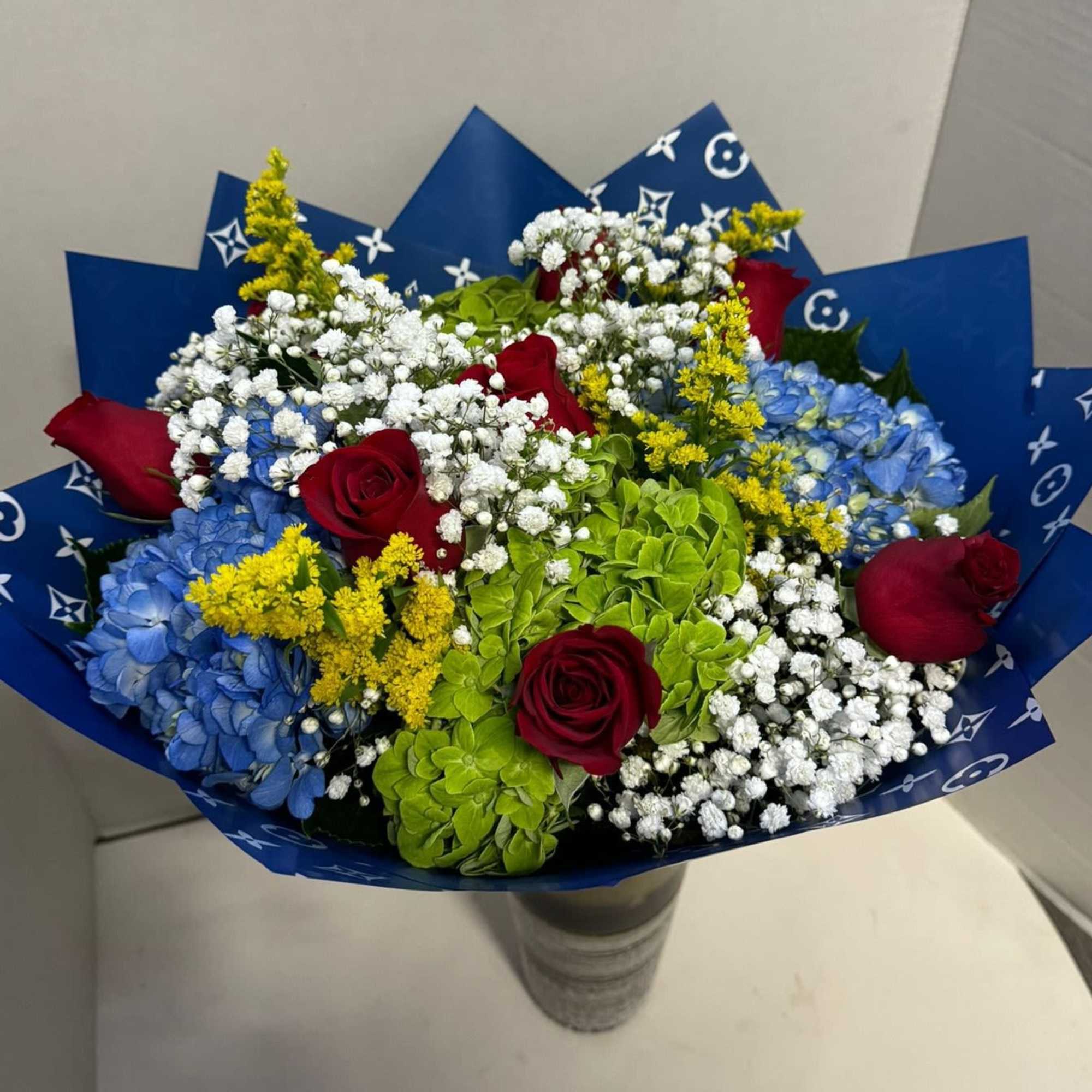 Bouquet of red roses, blue hydrangeas, and white baby's breath in blue wrap
