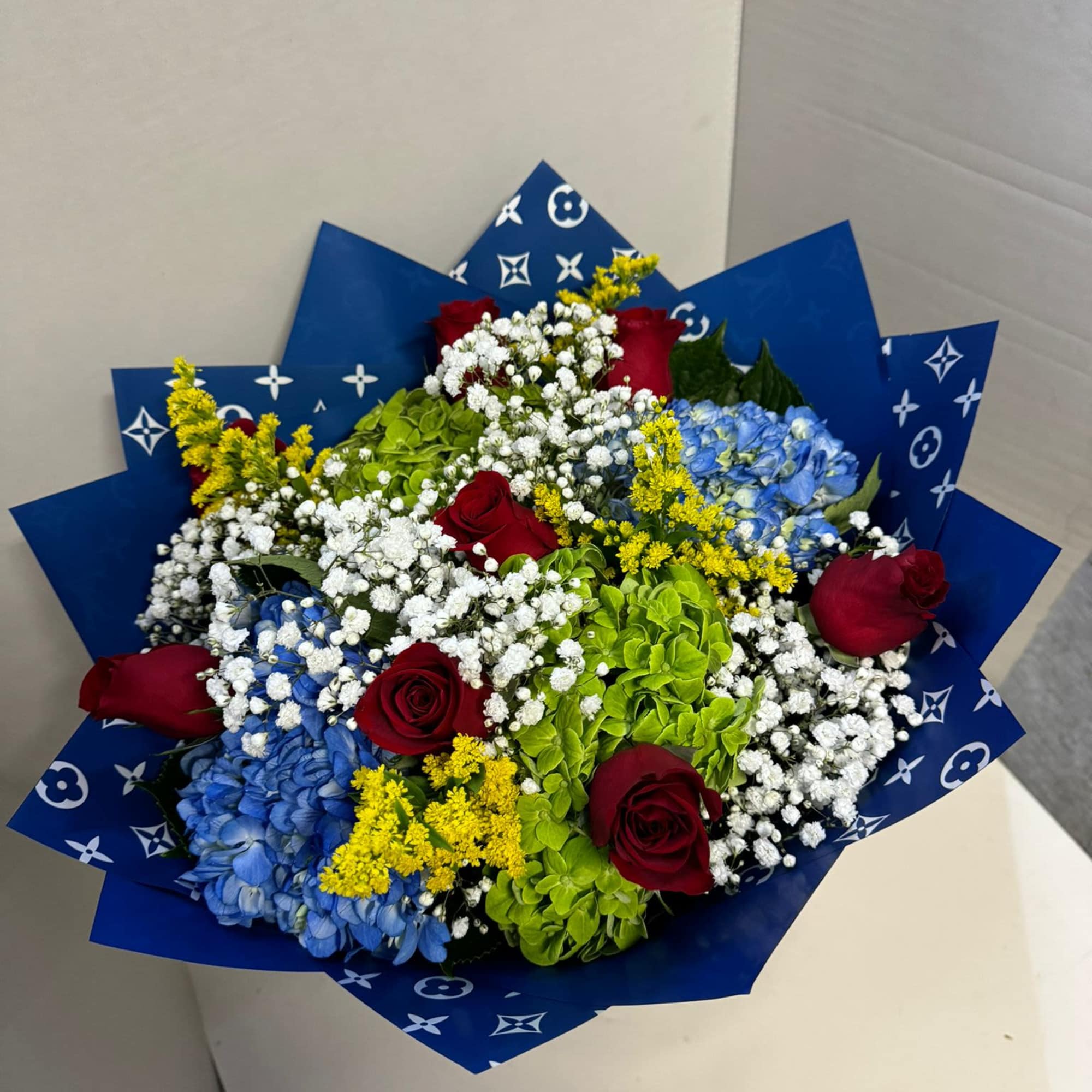 Bouquet of red roses, blue hydrangeas, and white baby's breath in blue wrap, photo 2 of 2