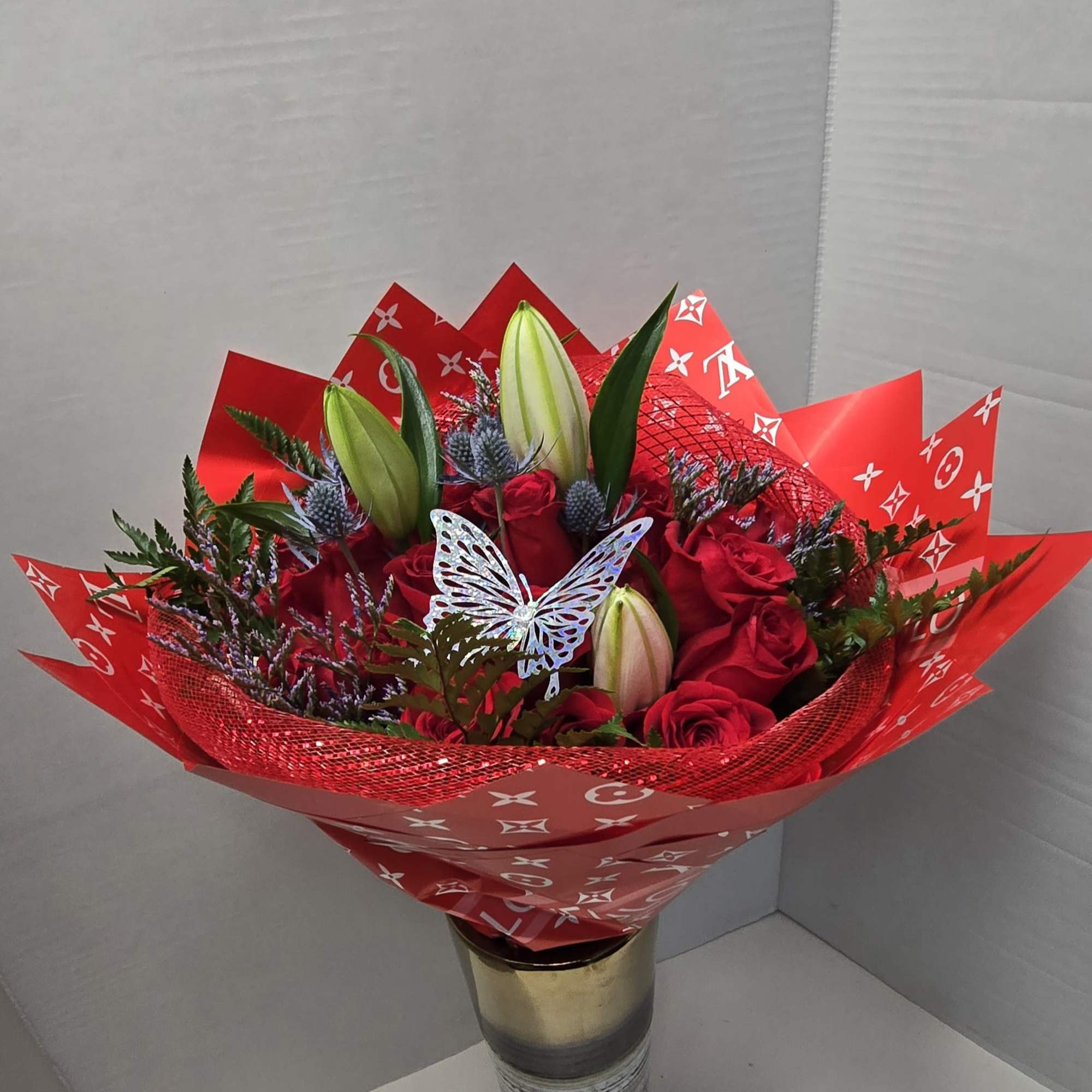 Red roses and lily buds in a gold vase with red wrapping