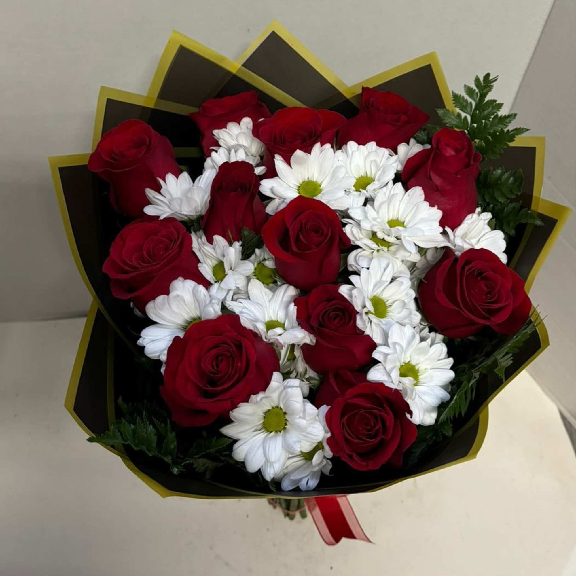 Bouquet of red roses and white daisies wrapped in black paper