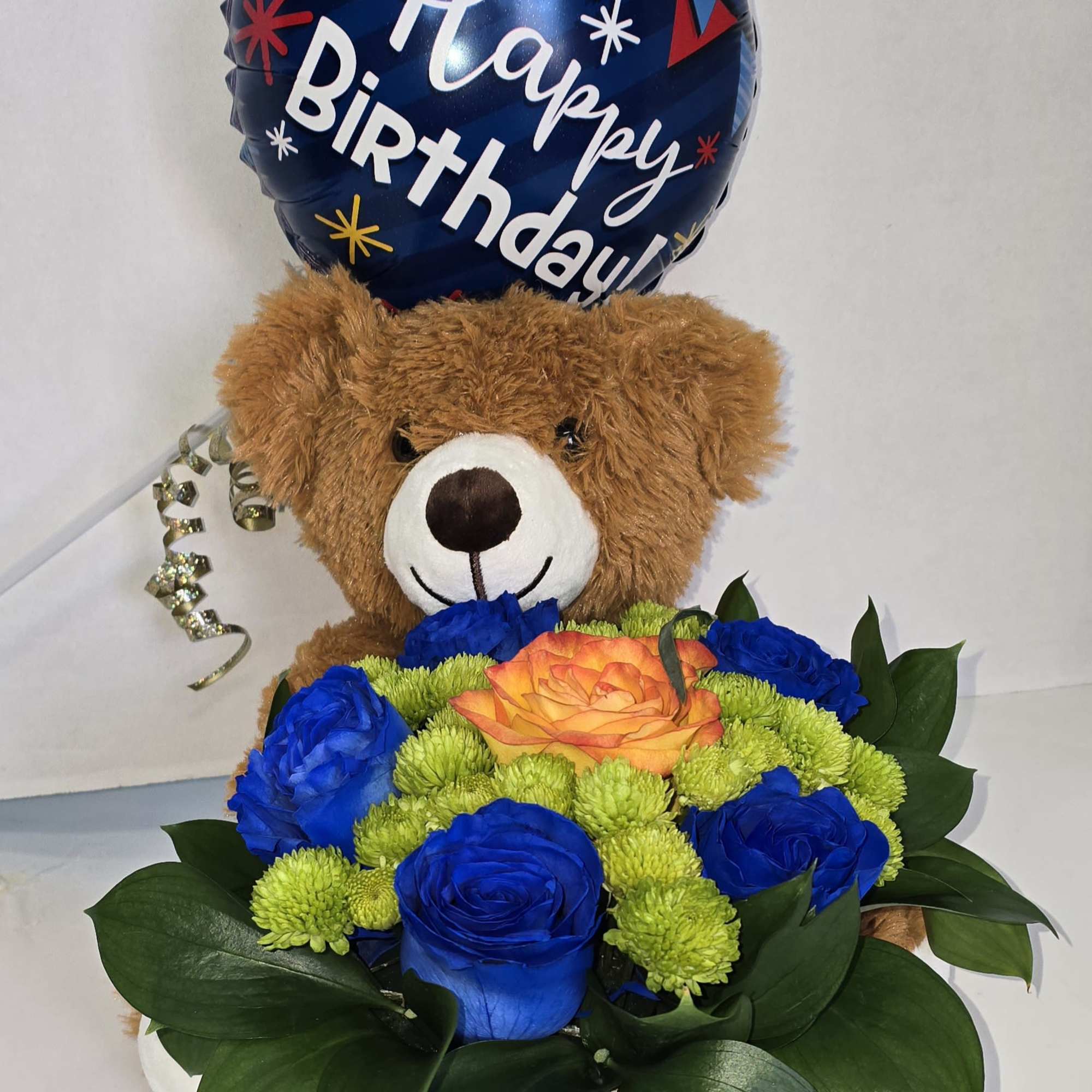 Birthday balloon above a teddy bear holding a basket of blue and orange flowers