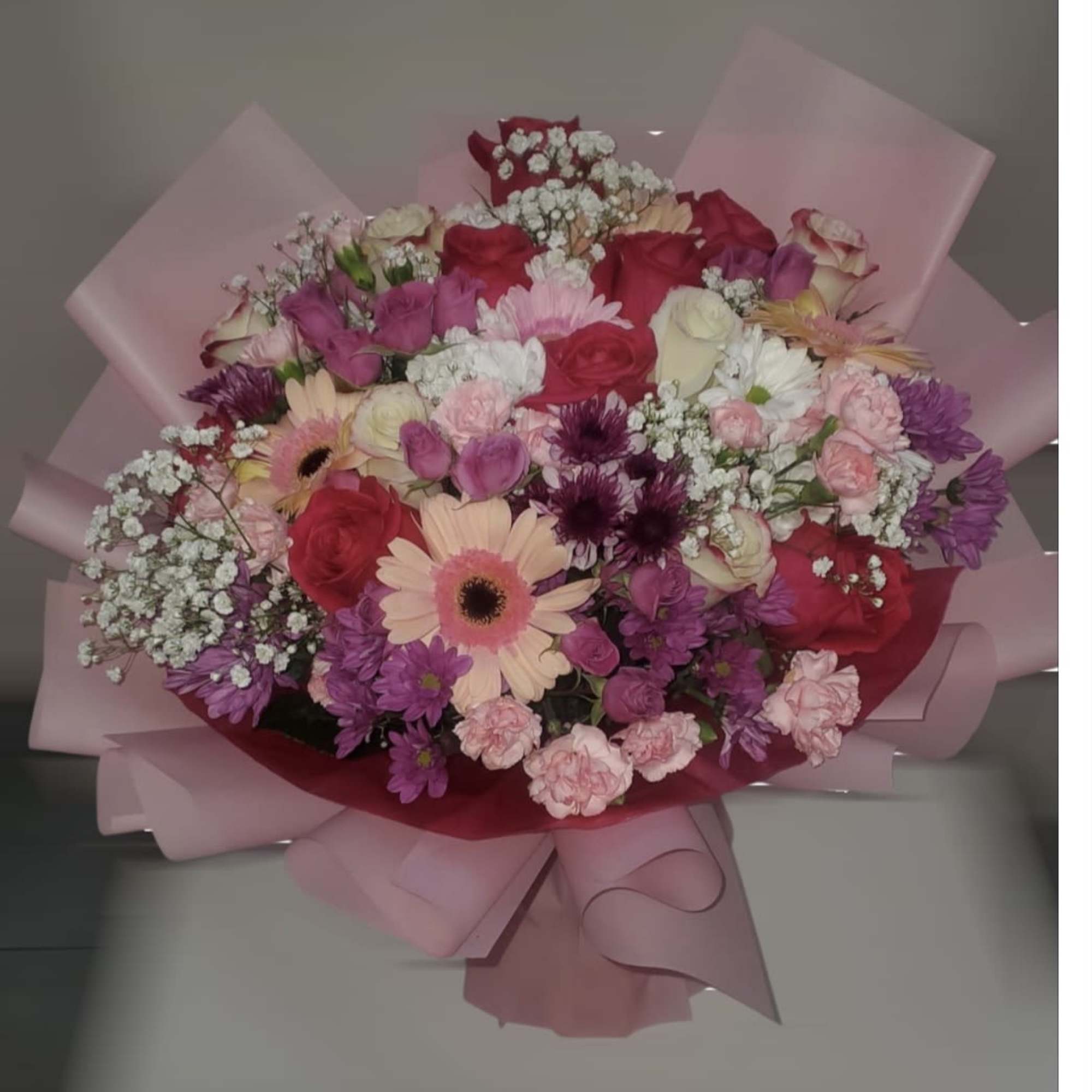 Mixed bouquet of pink, red, and white flowers wrapped in pink paper