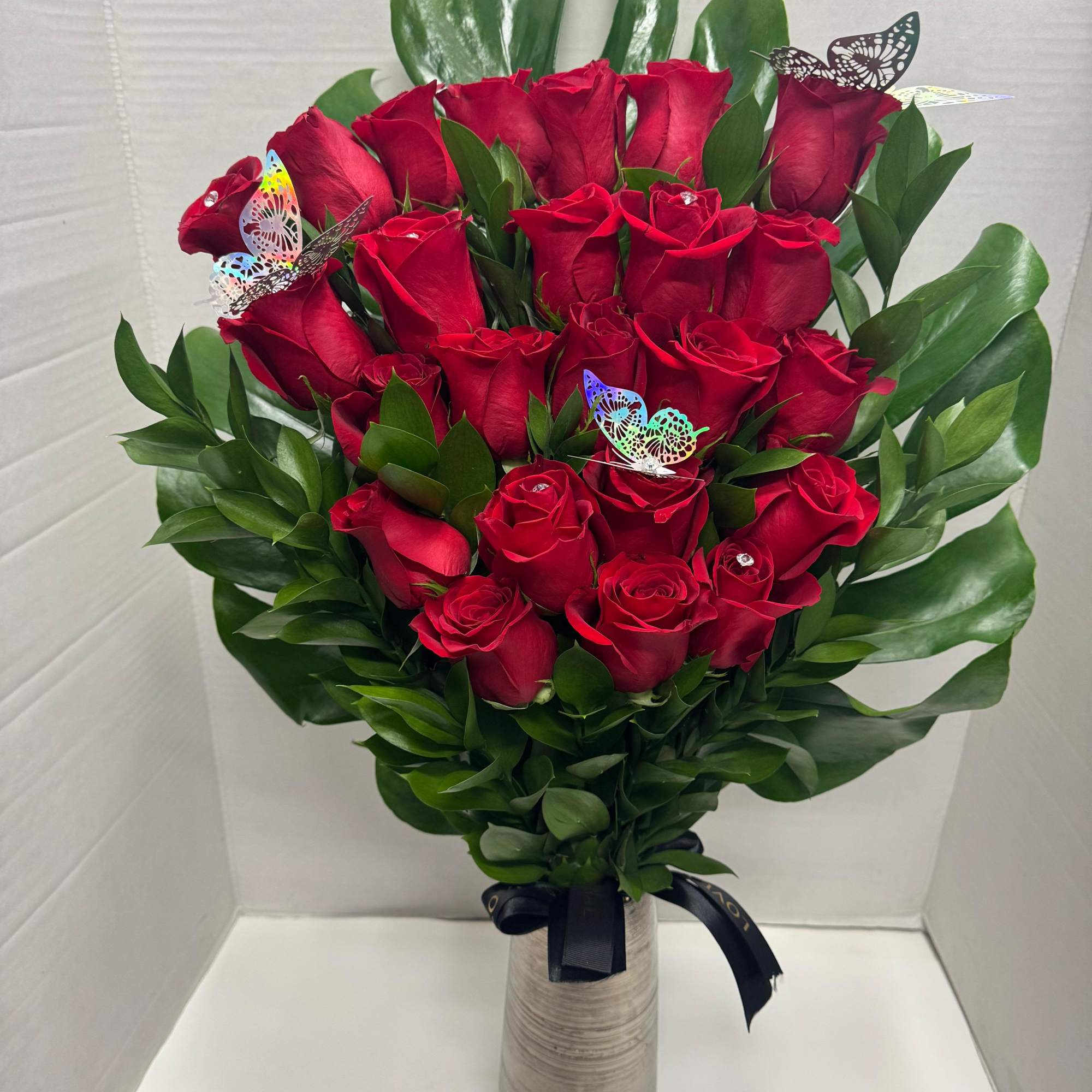 Bouquet of red roses in a tall vase with green leaves and butterfly picks