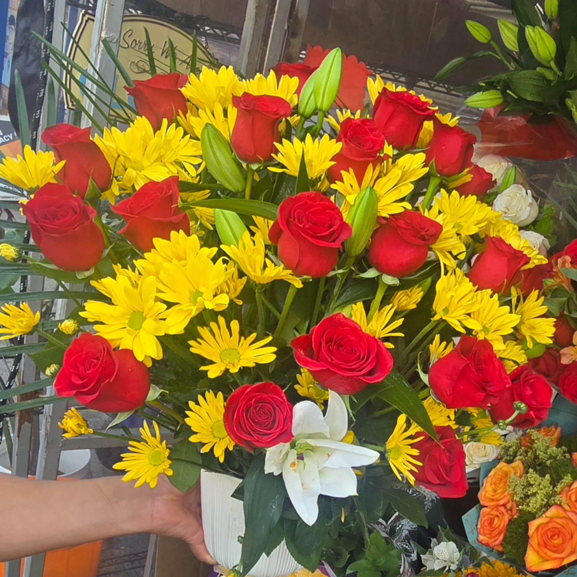 Bouquet of red roses, yellow daisies, and a white lily in a white vase