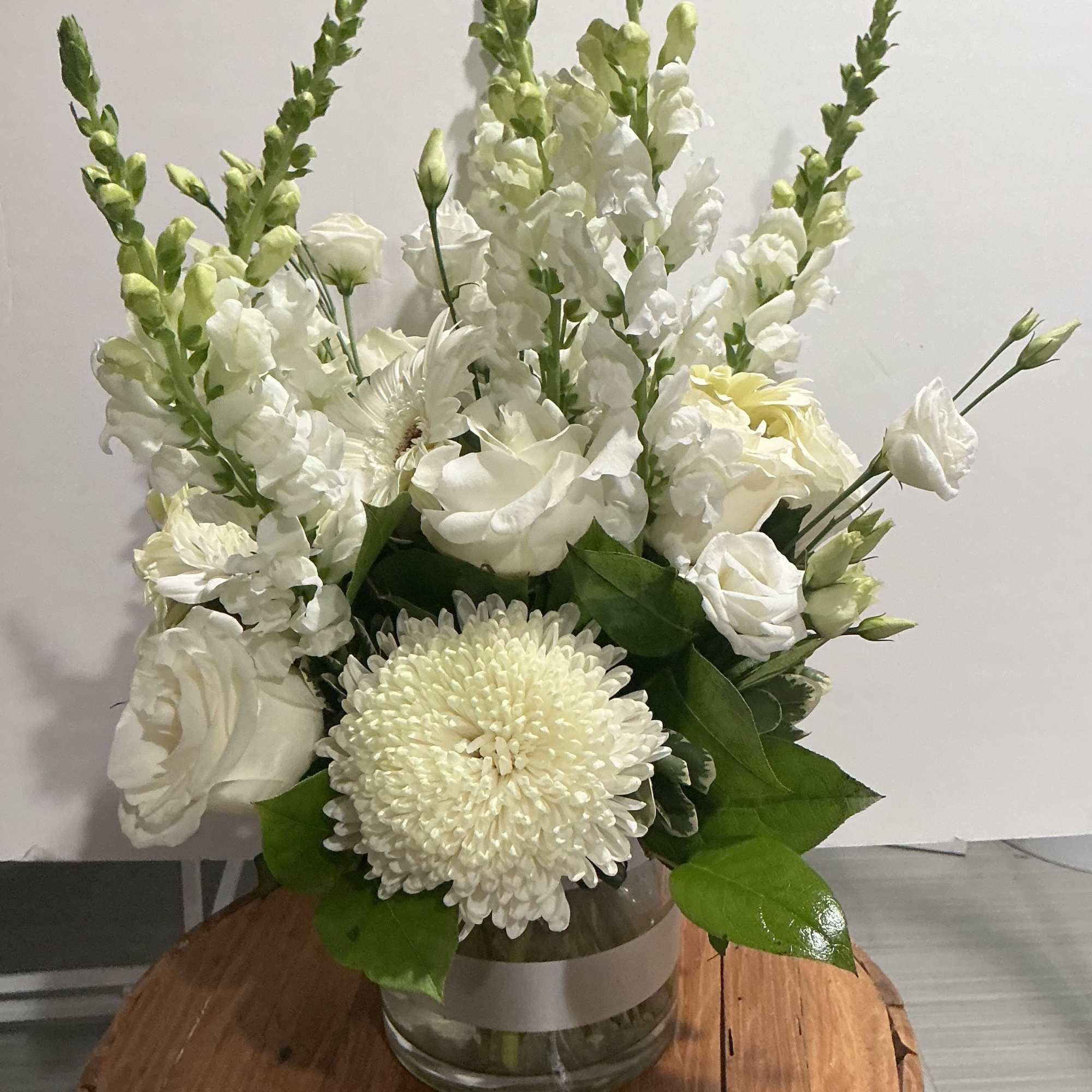 White floral arrangement in a glass vase with tall snapdragons and chrysanthemums