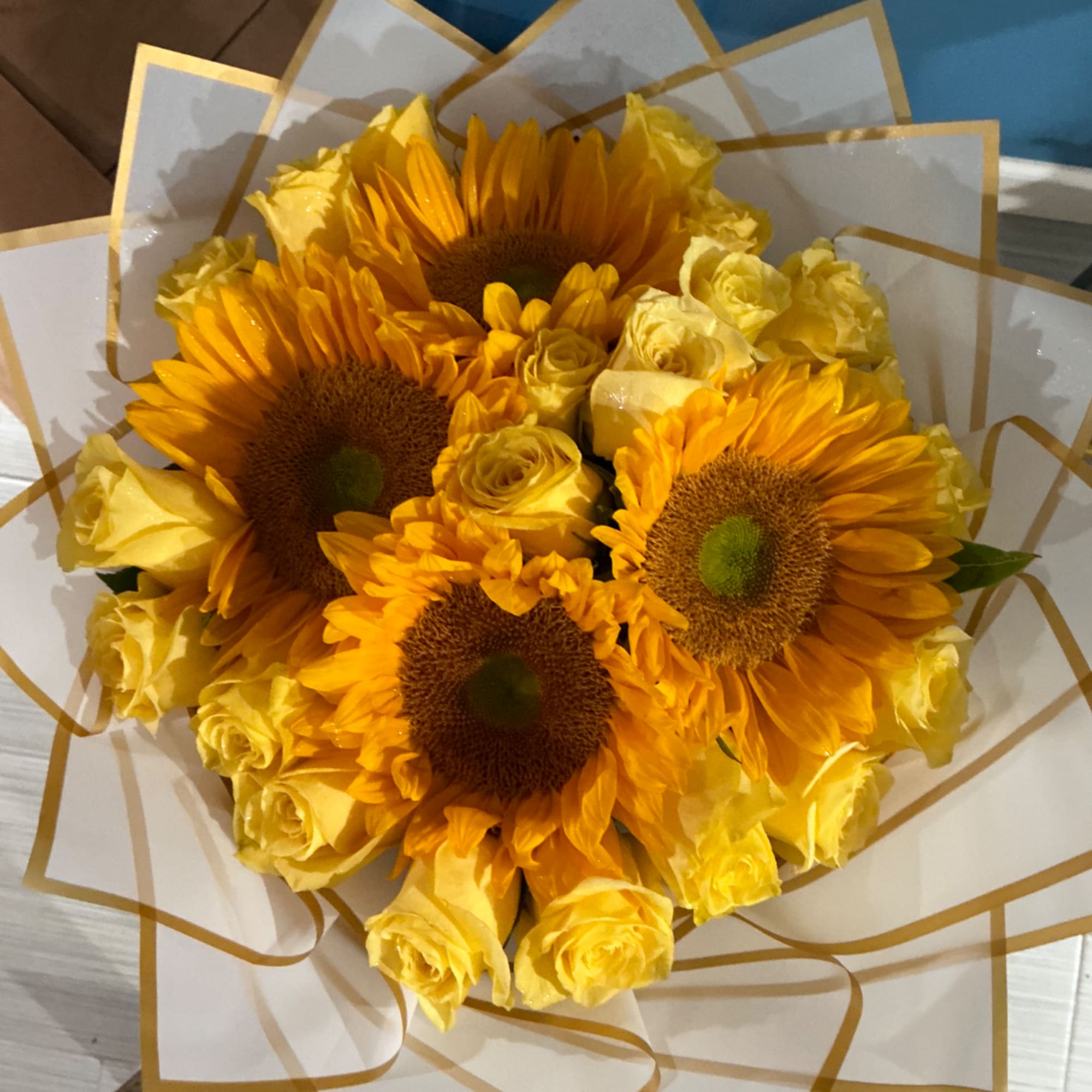 Bouquet of yellow sunflowers and roses wrapped in white paper with gold trim