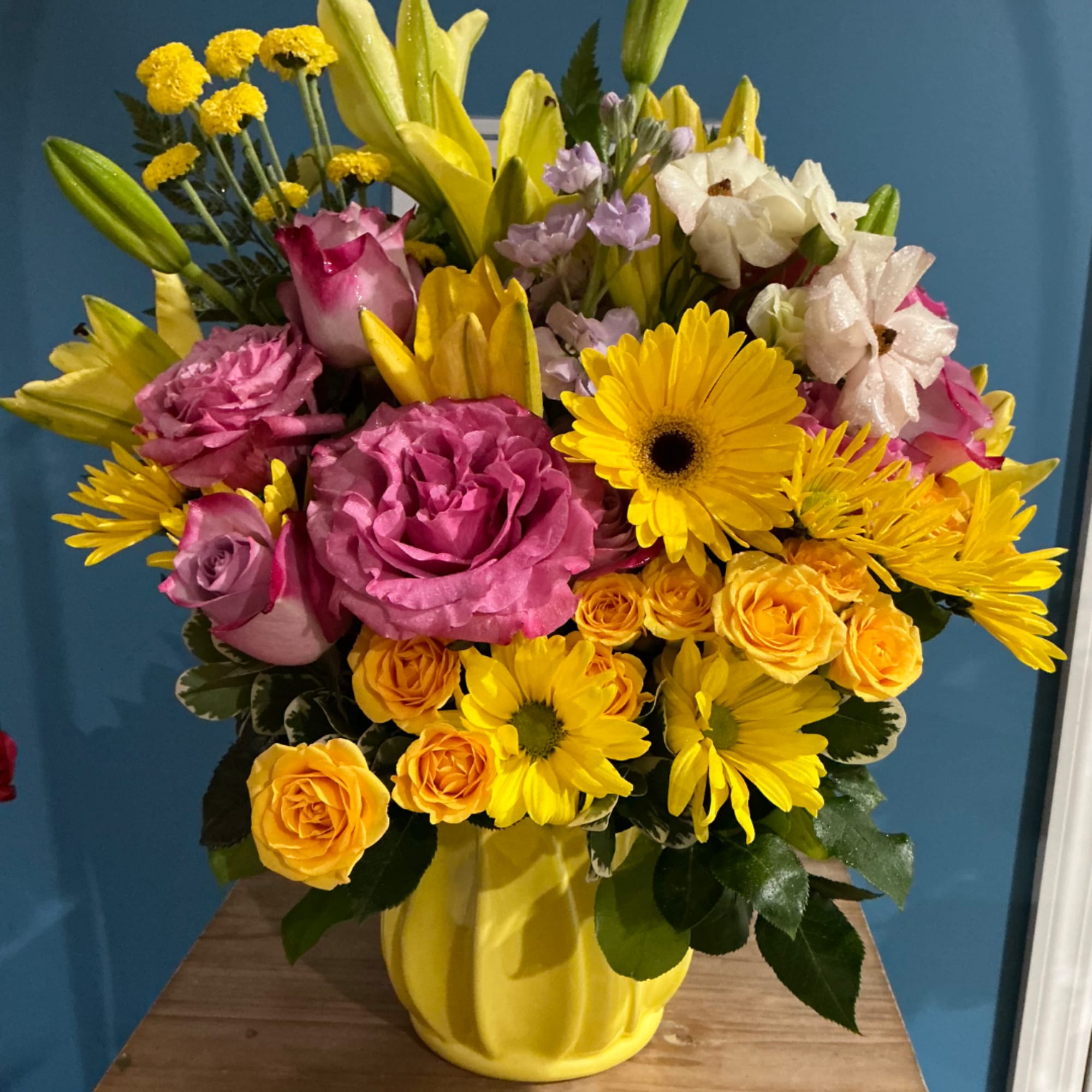 Colorful bouquet of roses, lilies, and daisies in a yellow vase