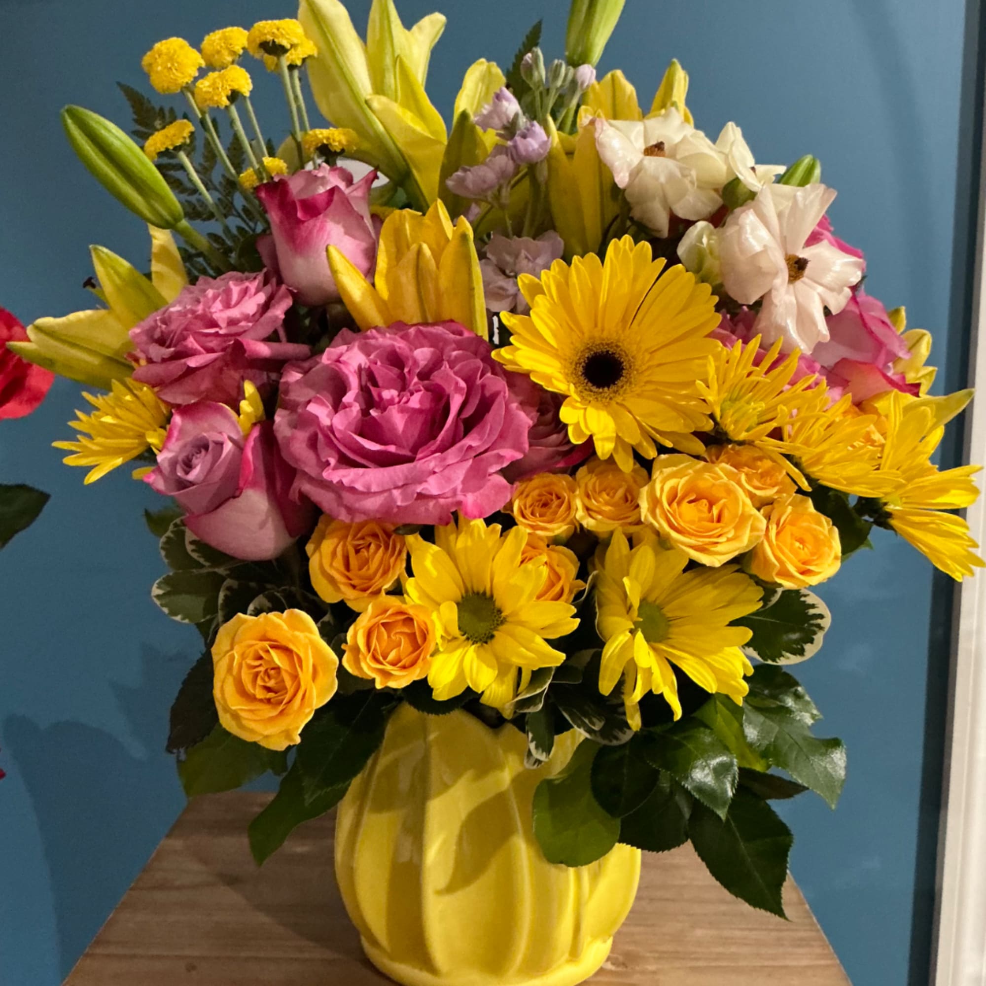 Bright mixed bouquet in a yellow vase with roses, lilies, and daisies