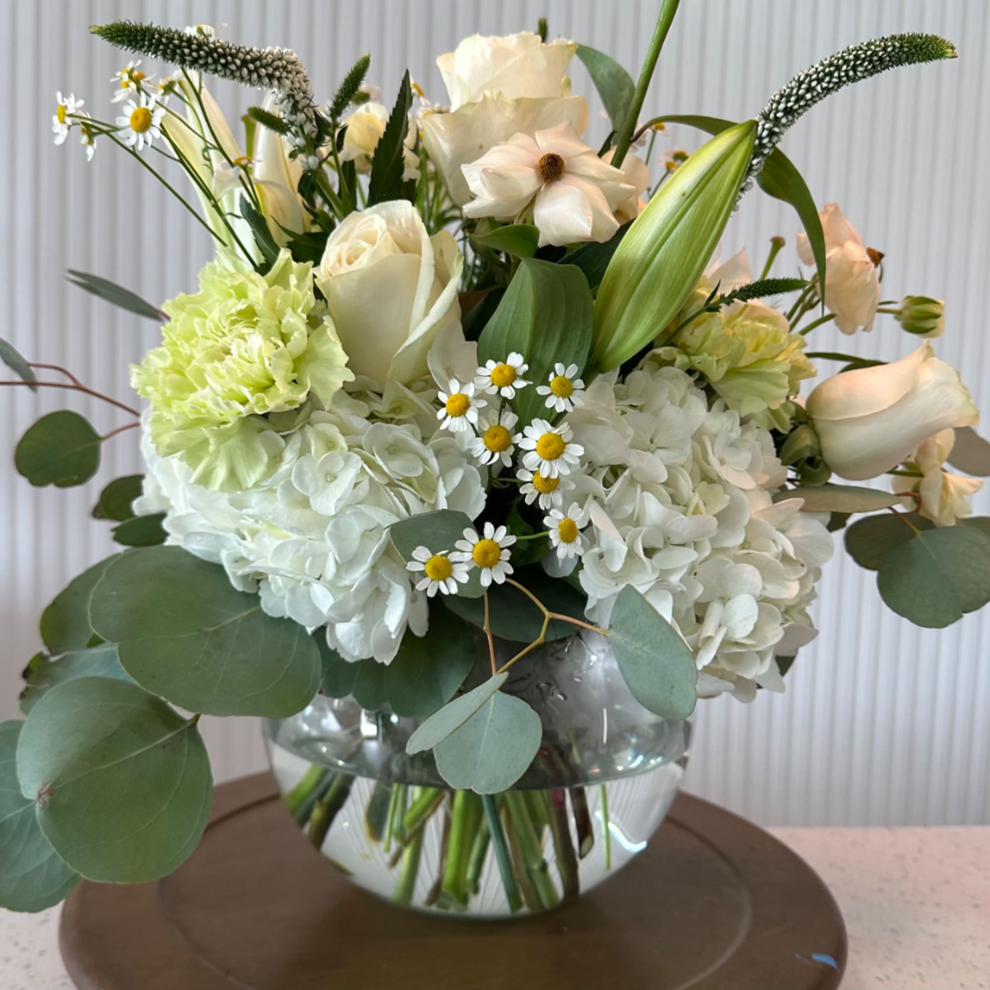 White floral arrangement in a clear glass vase with green foliage