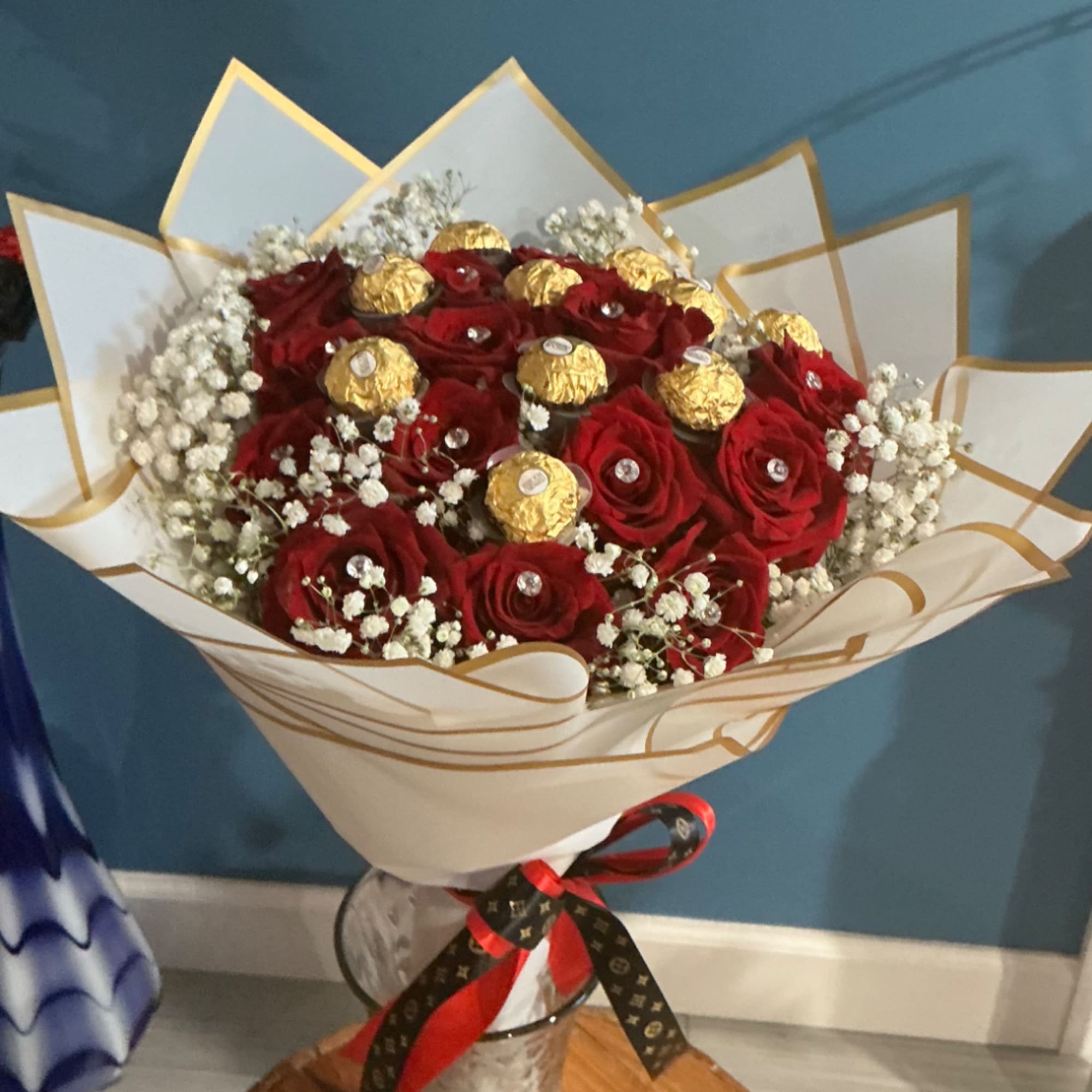Bouquet of red roses with gold-wrapped chocolates and white baby's breath in paper wrap