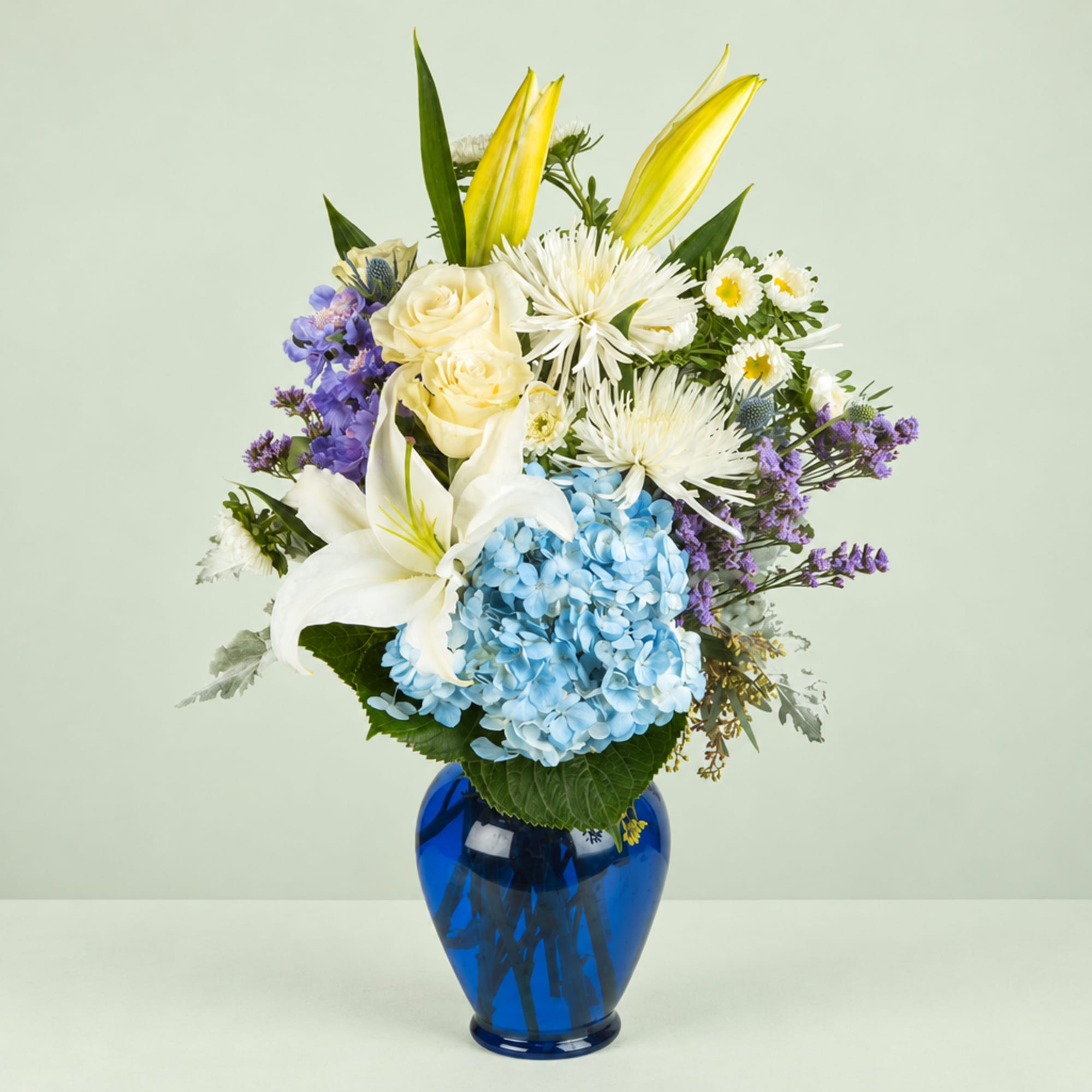 Bouquet of lilies, roses, hydrangea, and purple flowers in a blue vase