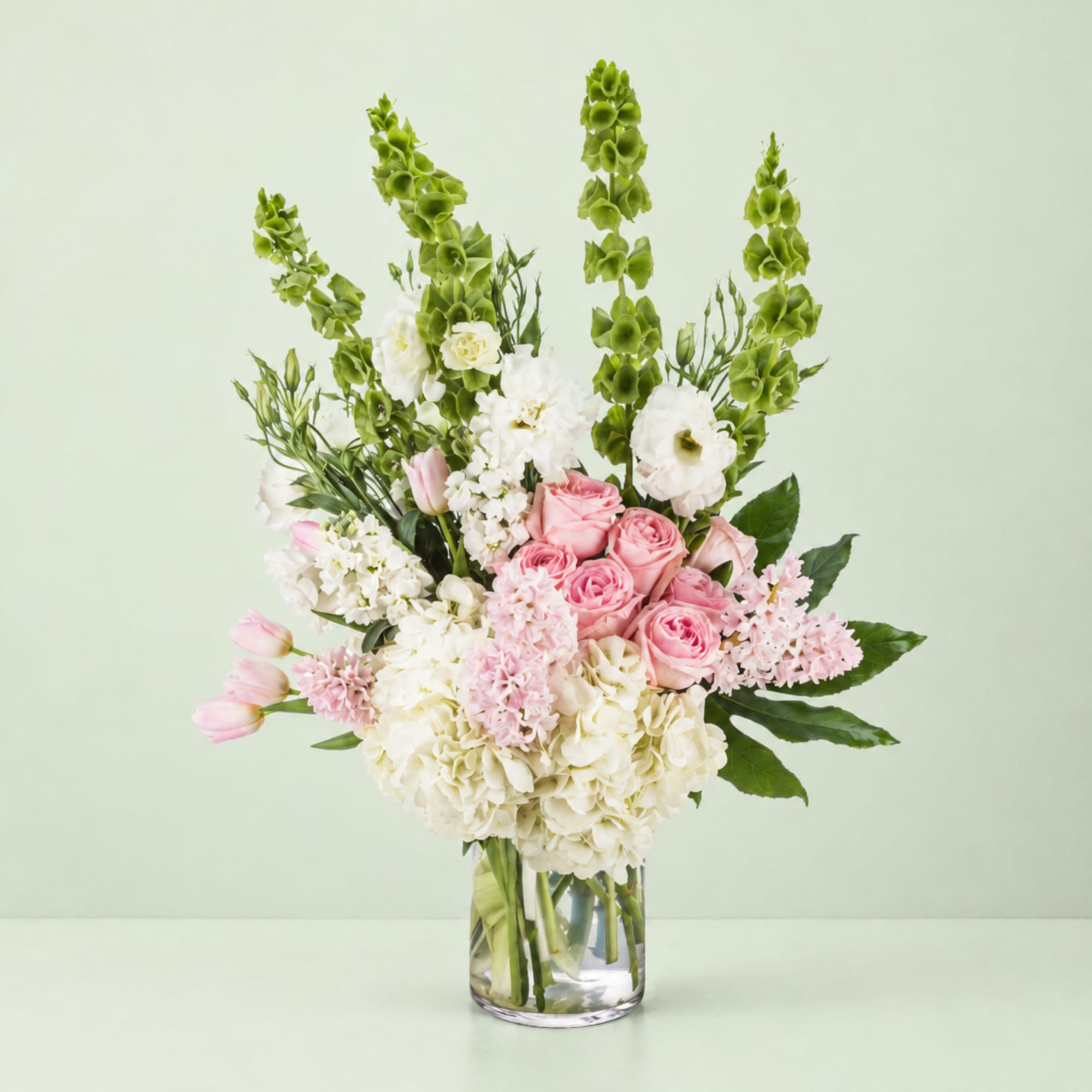 Pink and white bouquet in a clear glass vase with tall green spikes