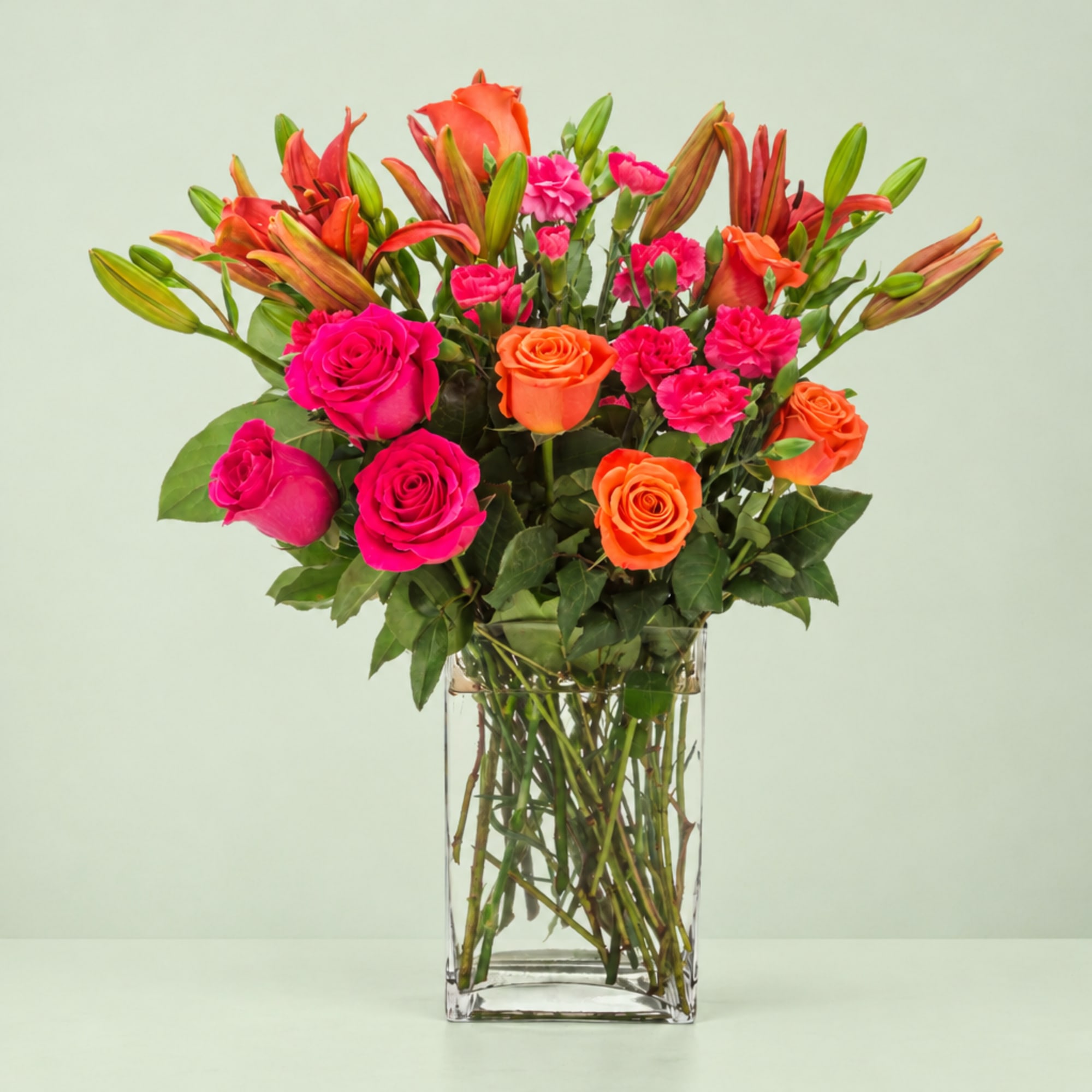 Pink and orange roses with lilies in a clear glass vase