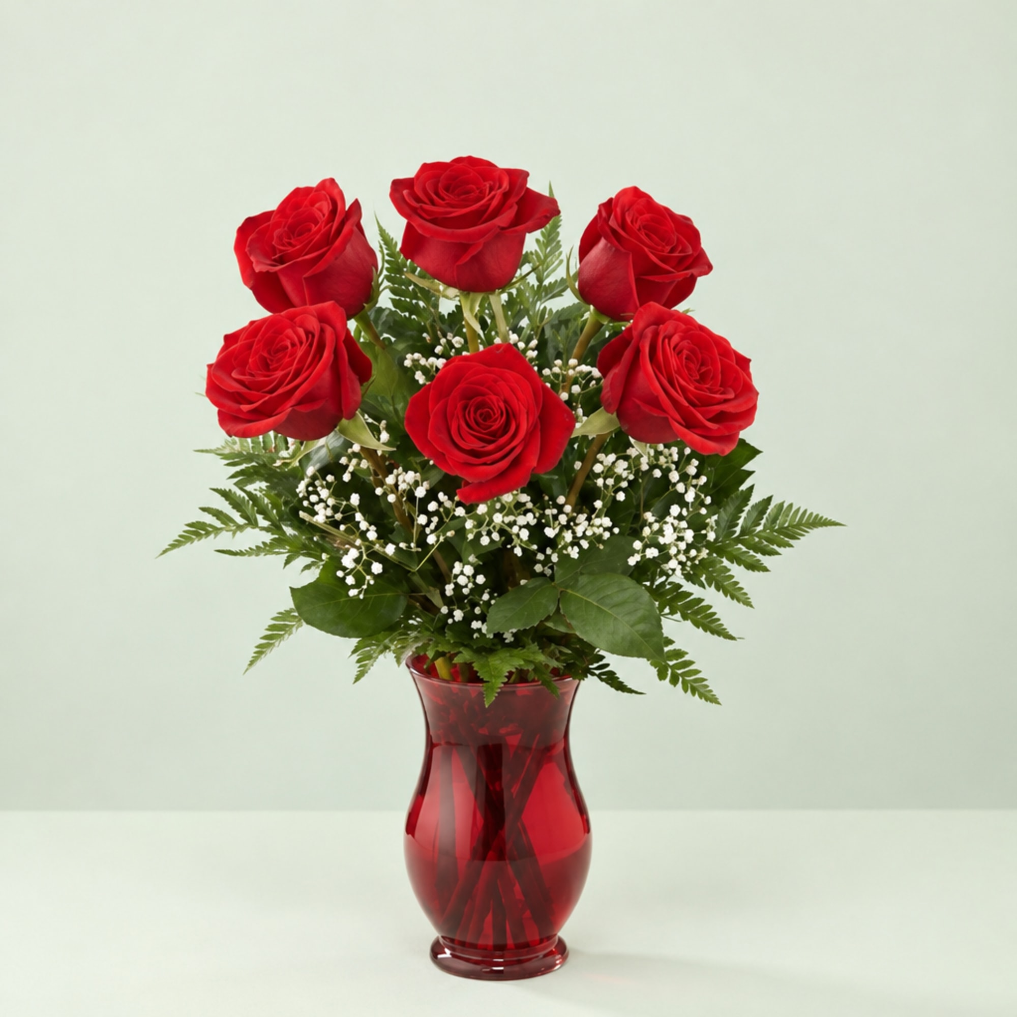 Red roses arranged in a red glass vase with baby's breath