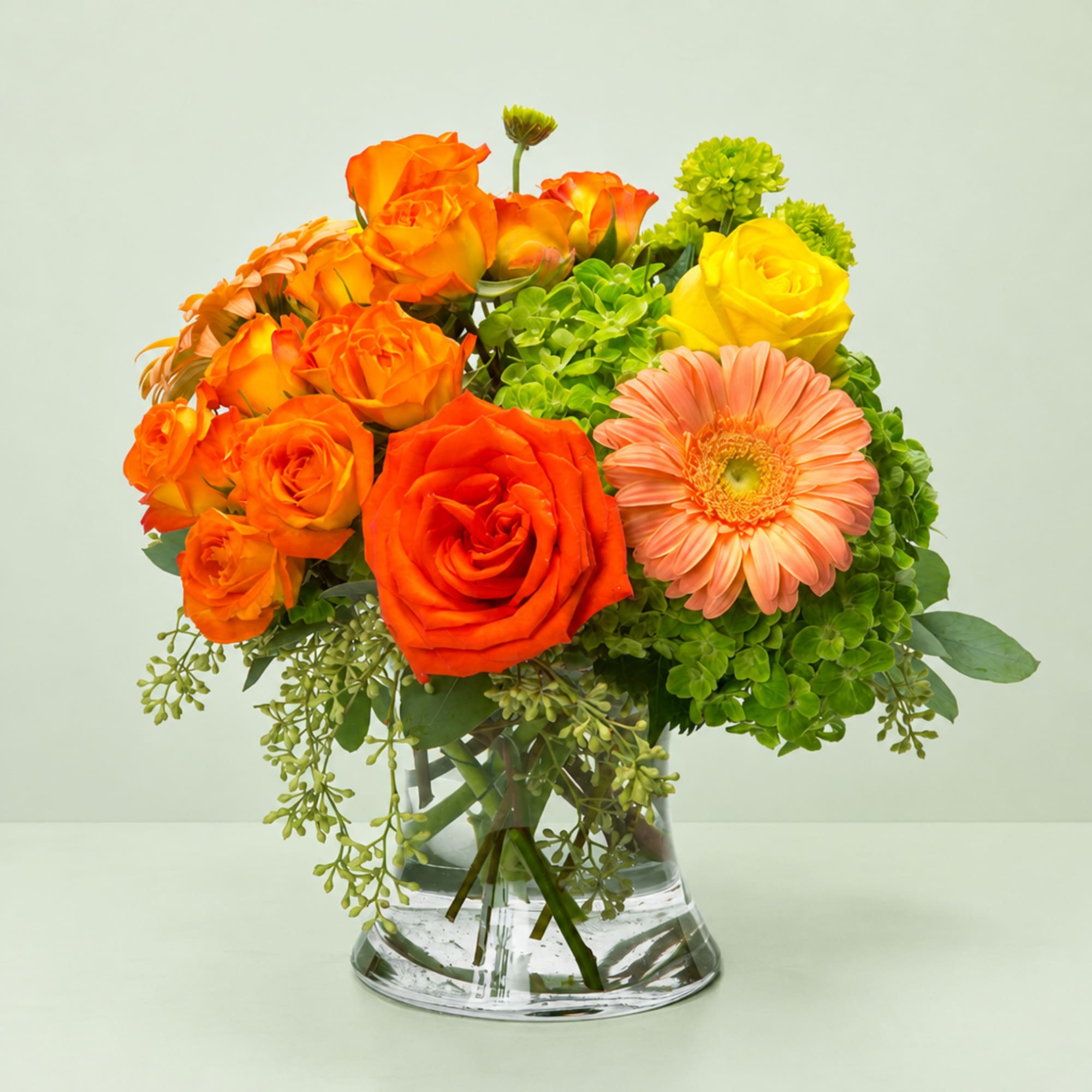 Orange and yellow roses with a peach gerbera daisy in a glass vase