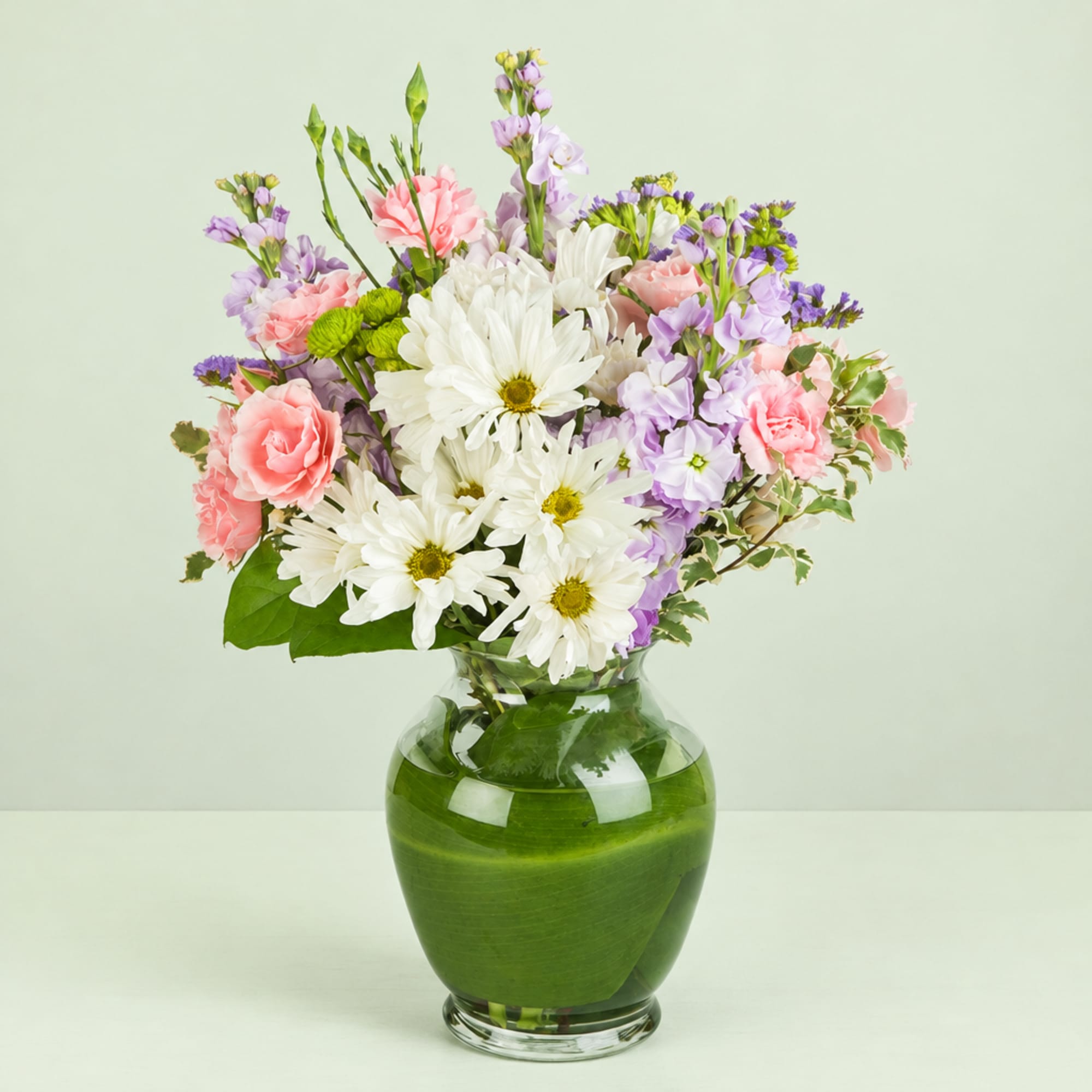 Bouquet of white daisies, pink carnations, and lavender flowers in a glass vase