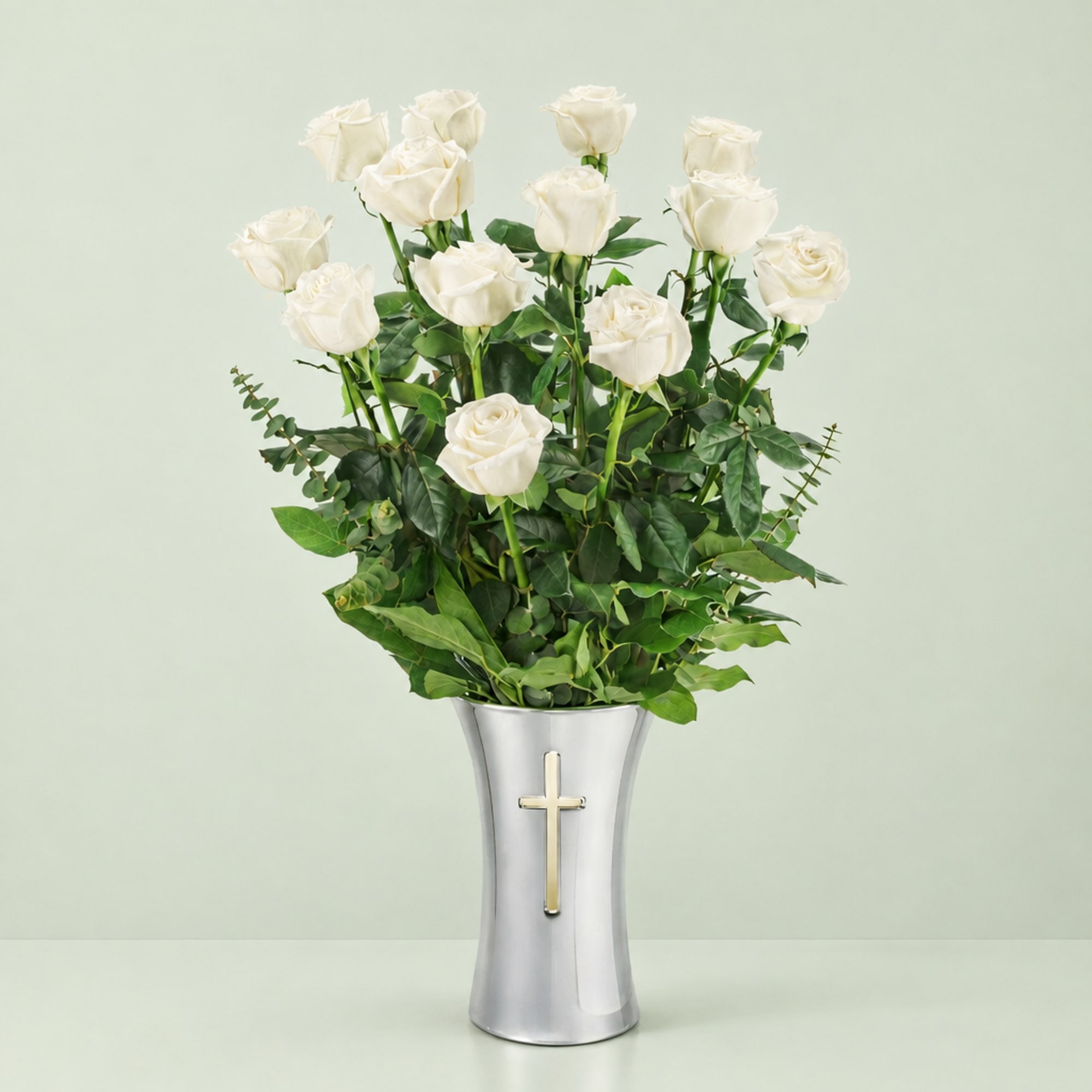White roses in a silver vase with a cross emblem
