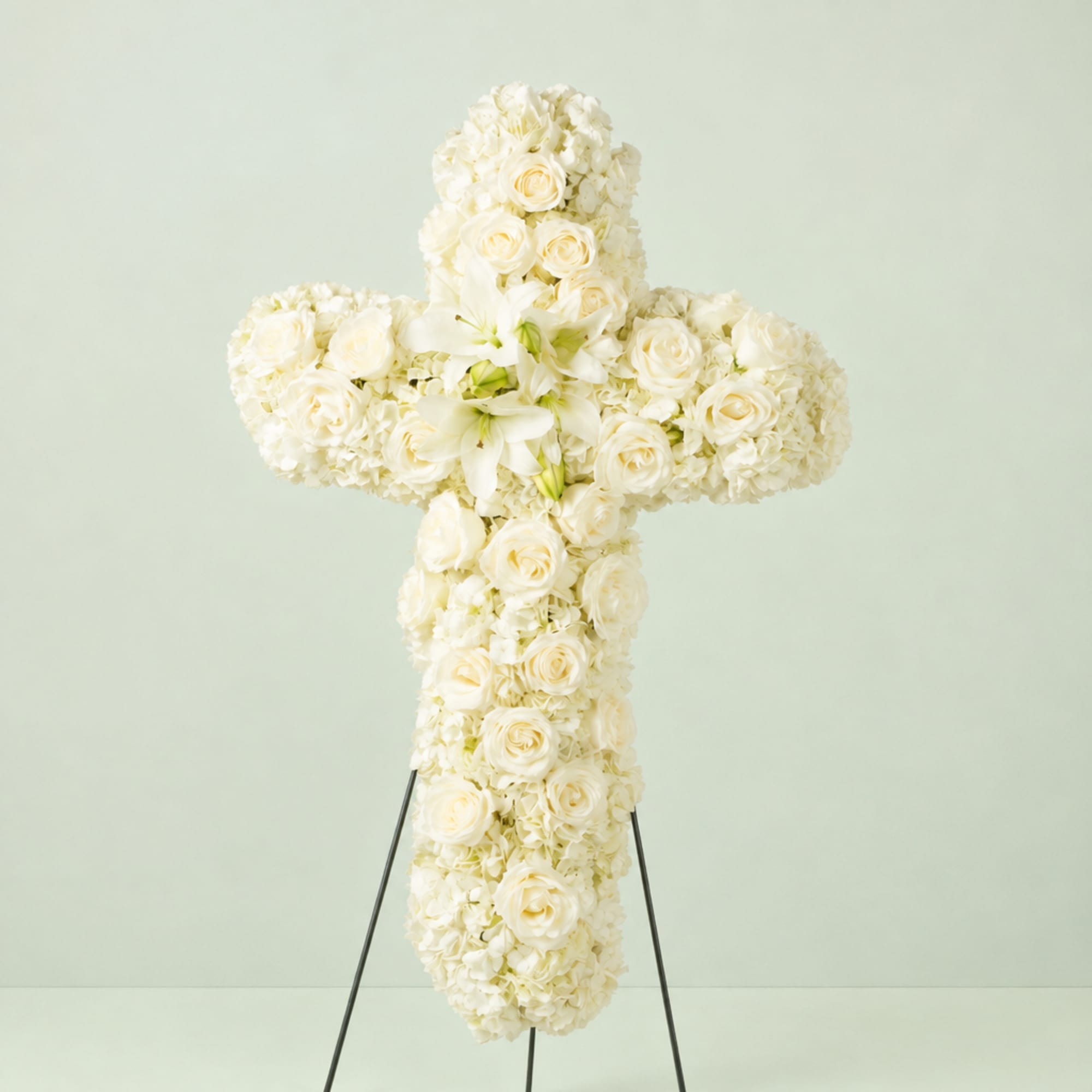 White floral cross on a stand with roses and lilies