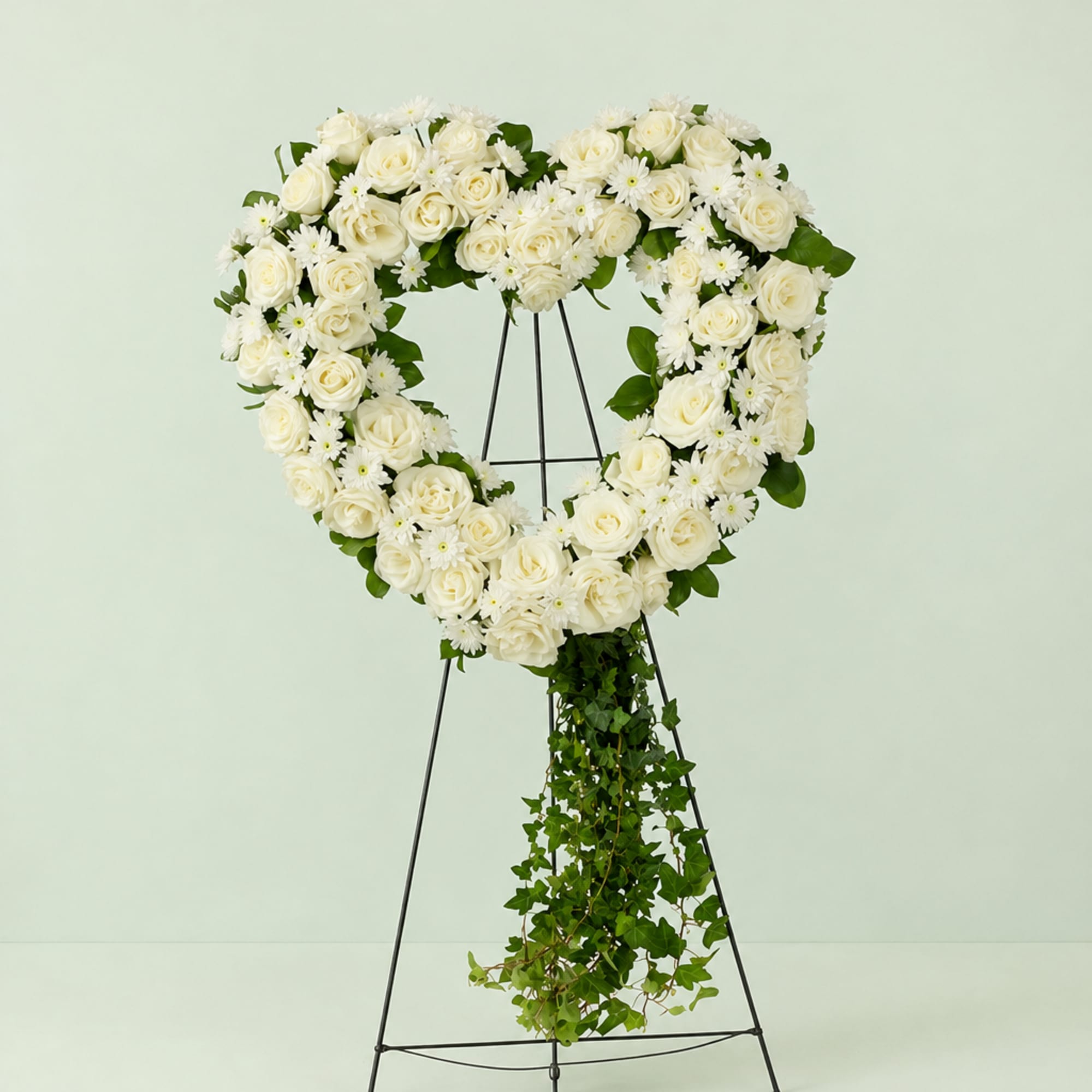 Heart-shaped white rose wreath on a stand with trailing ivy