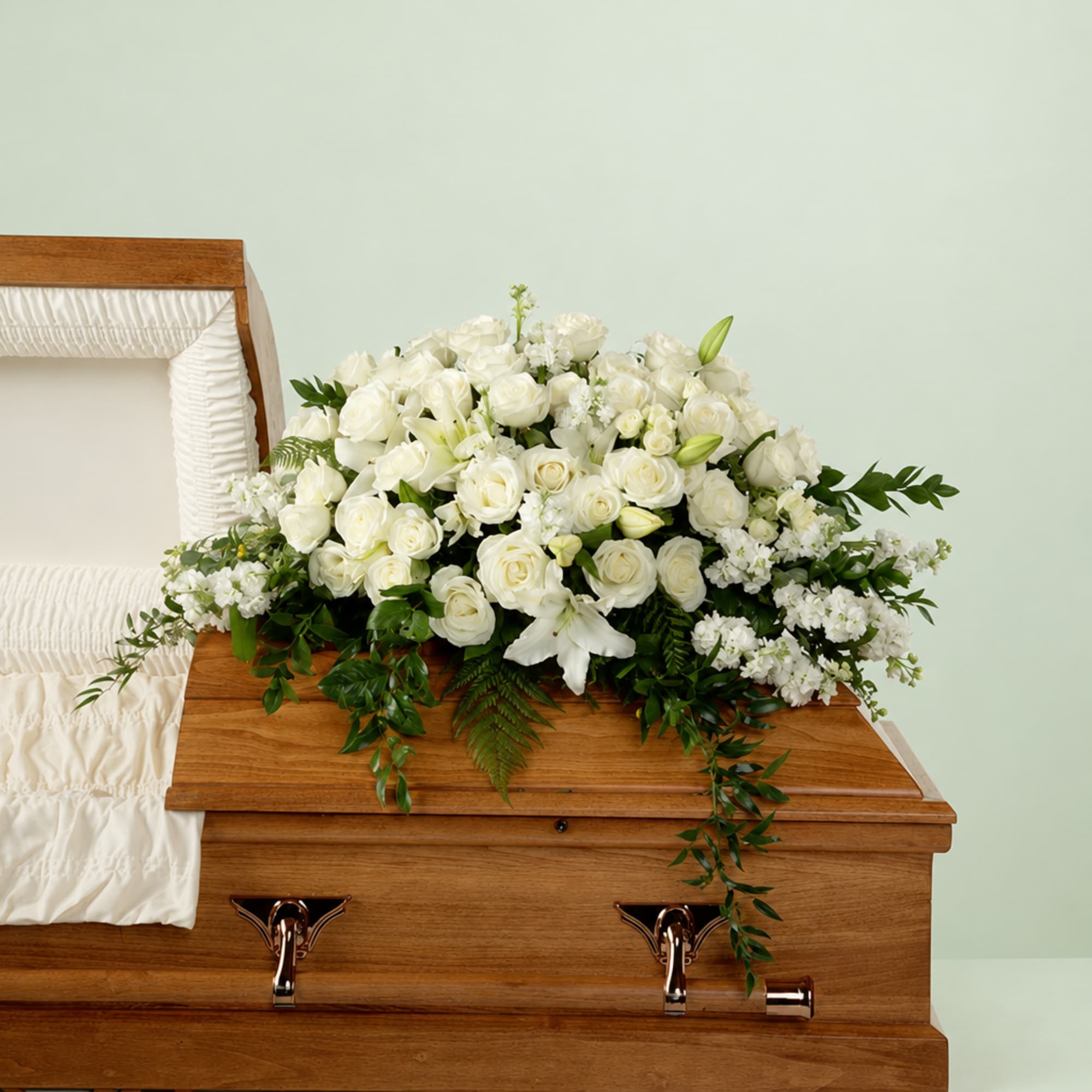 White floral casket spray with roses and lilies on a wooden casket