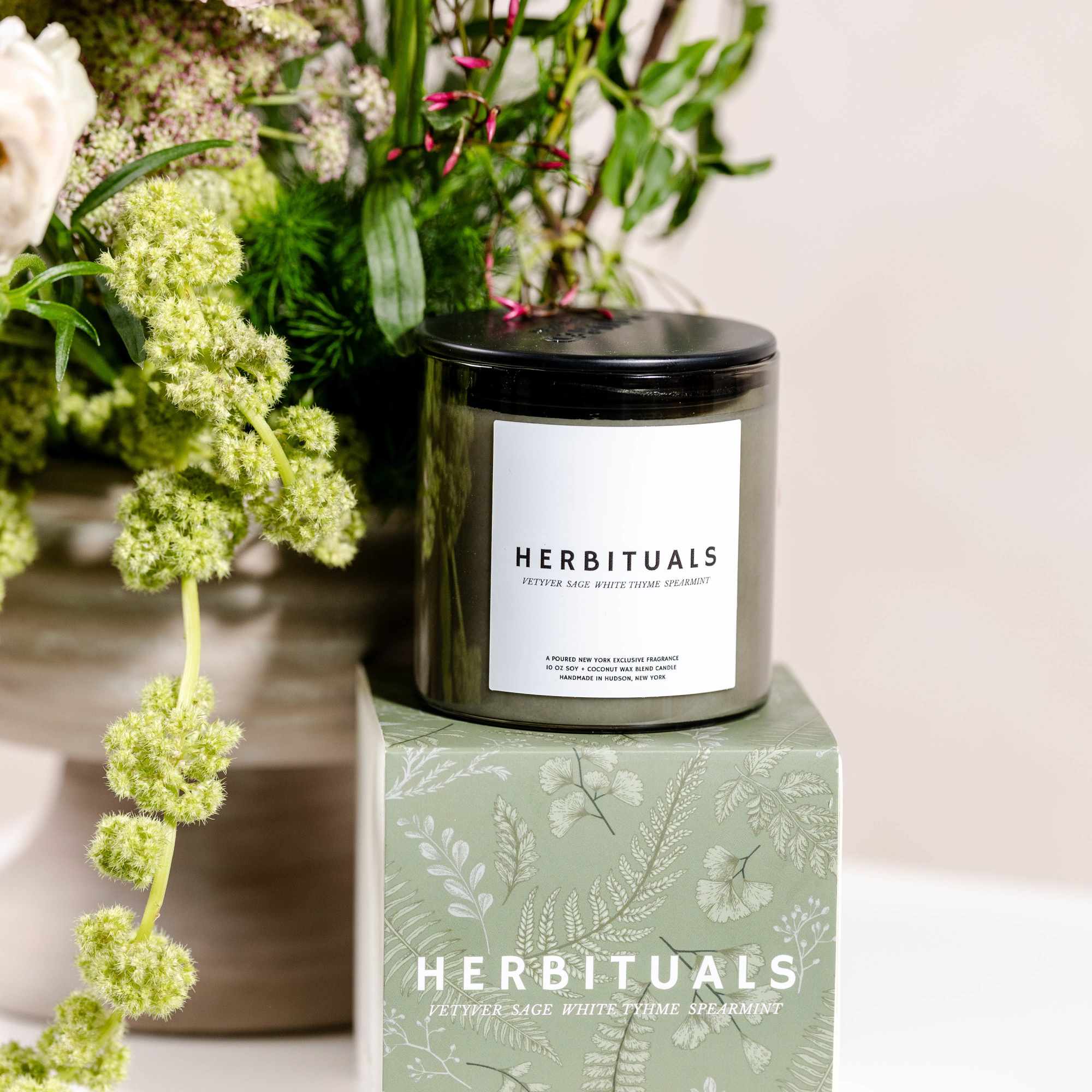Black candle on a patterned green box beside pale flowers