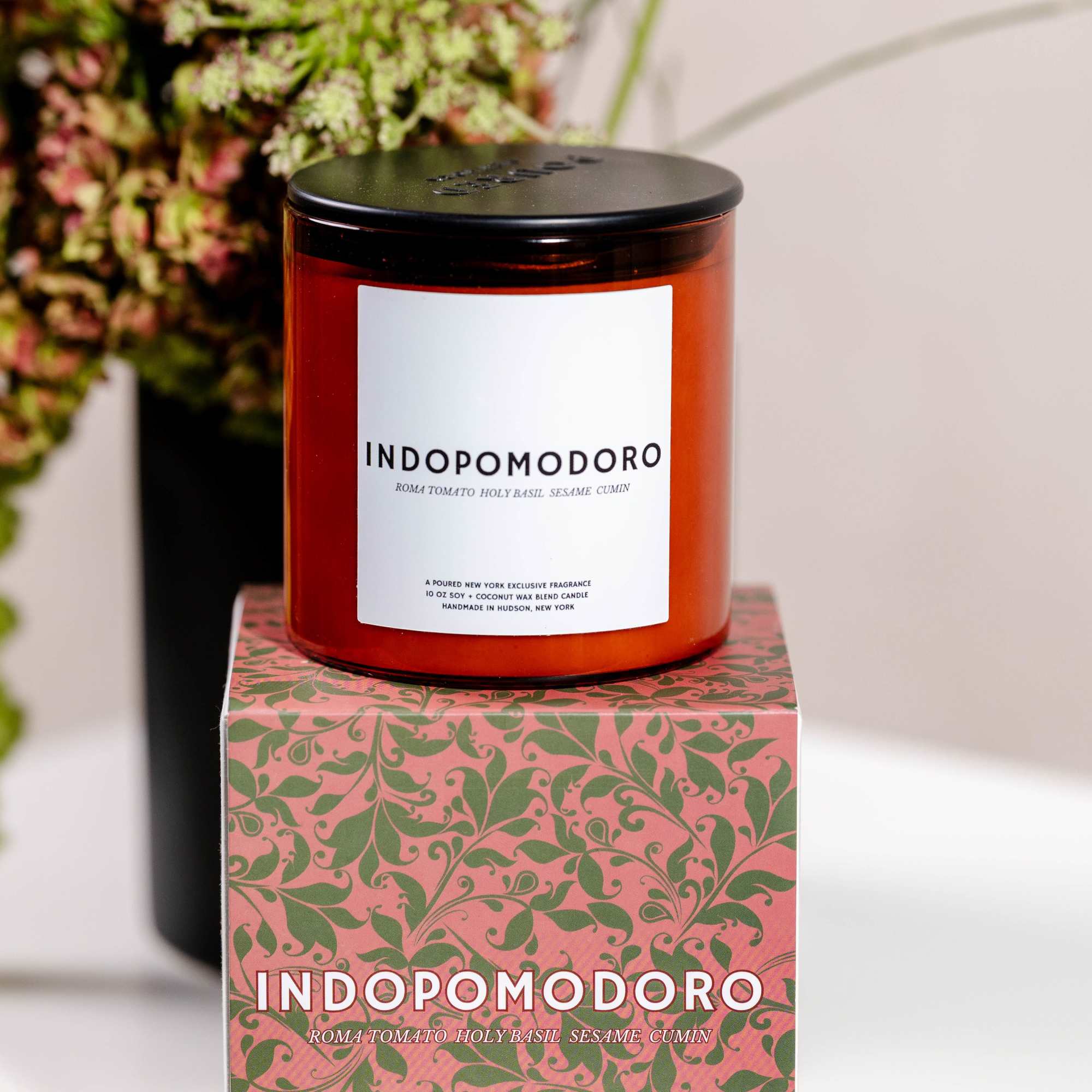 Amber candle jar on a patterned box with flowers blurred behind it