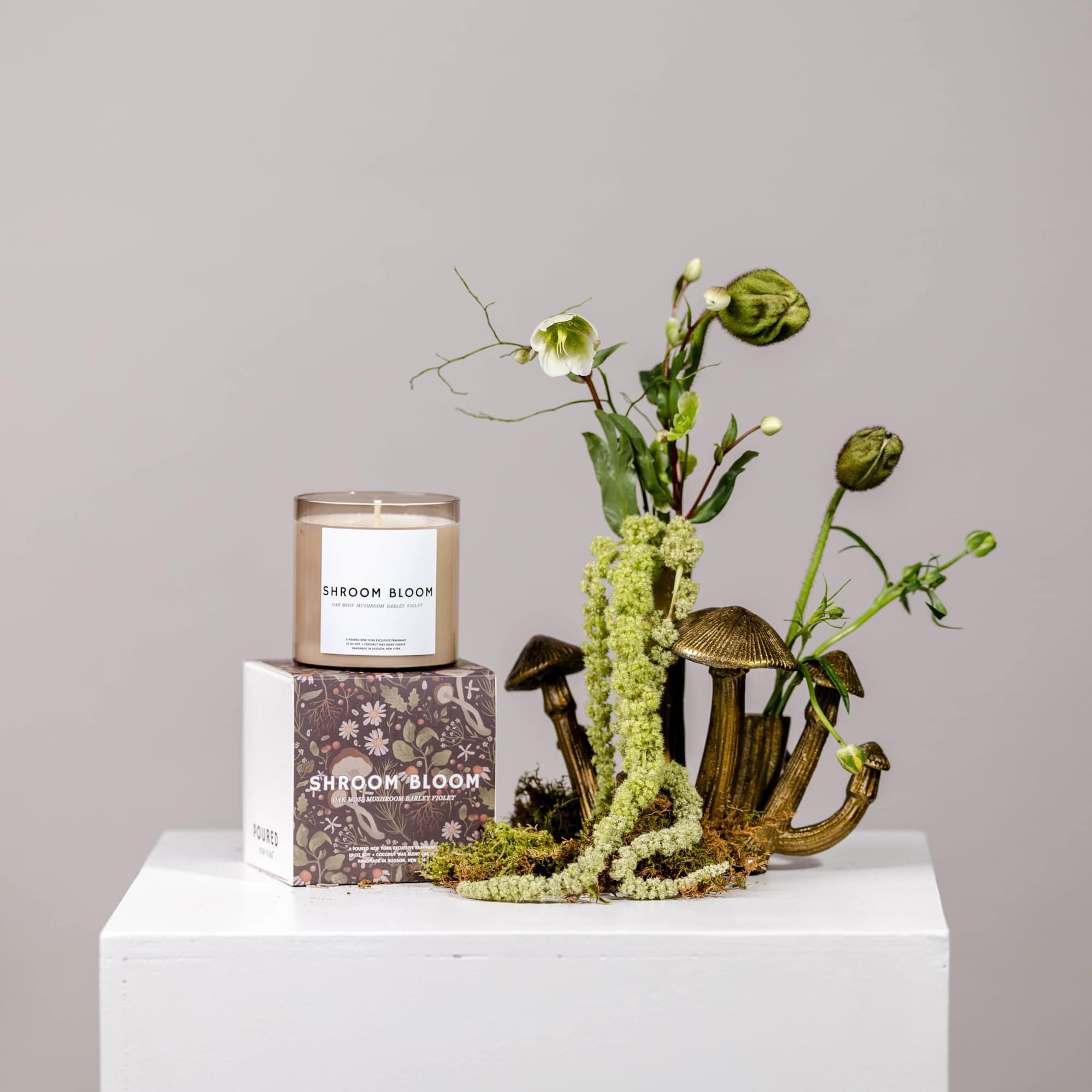 Candle in a box beside a small mushroom-shaped floral arrangement