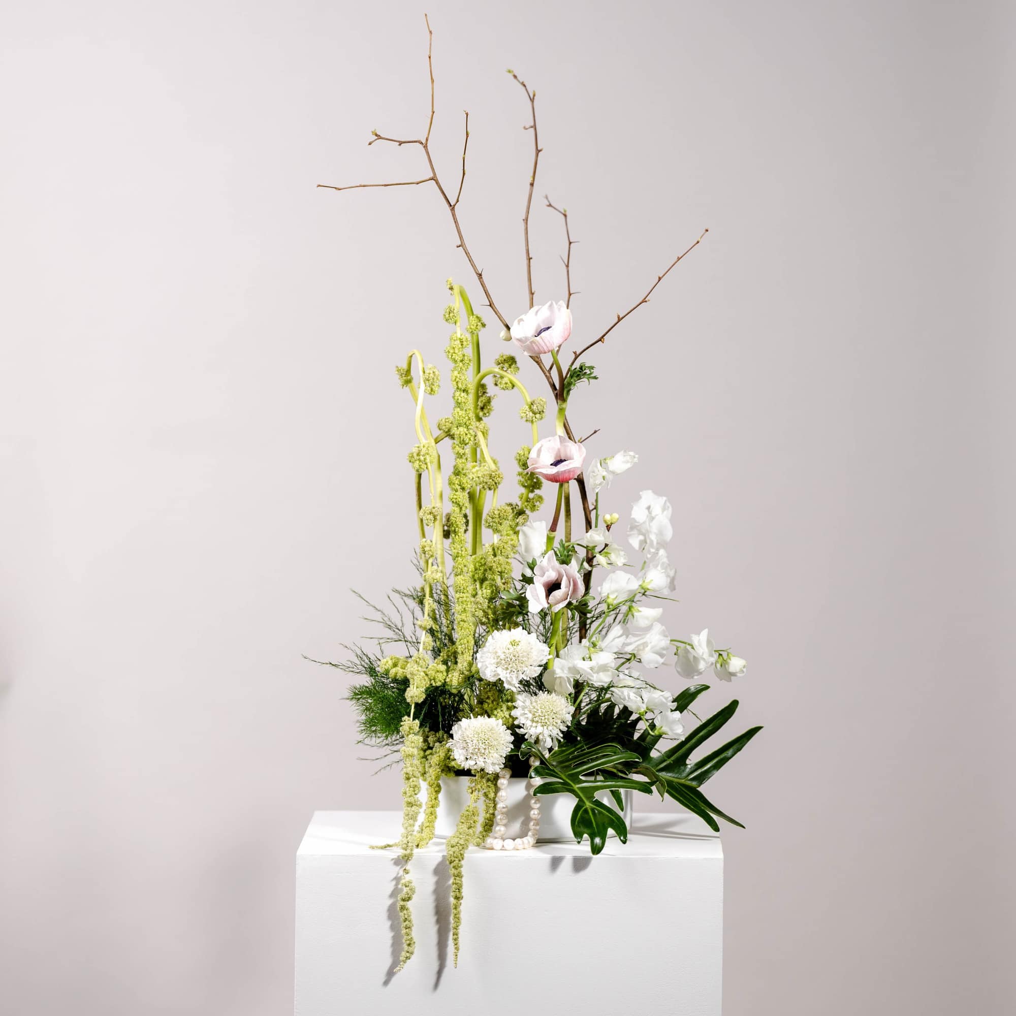 Tall floral arrangement with white and pale pink blooms in a white container