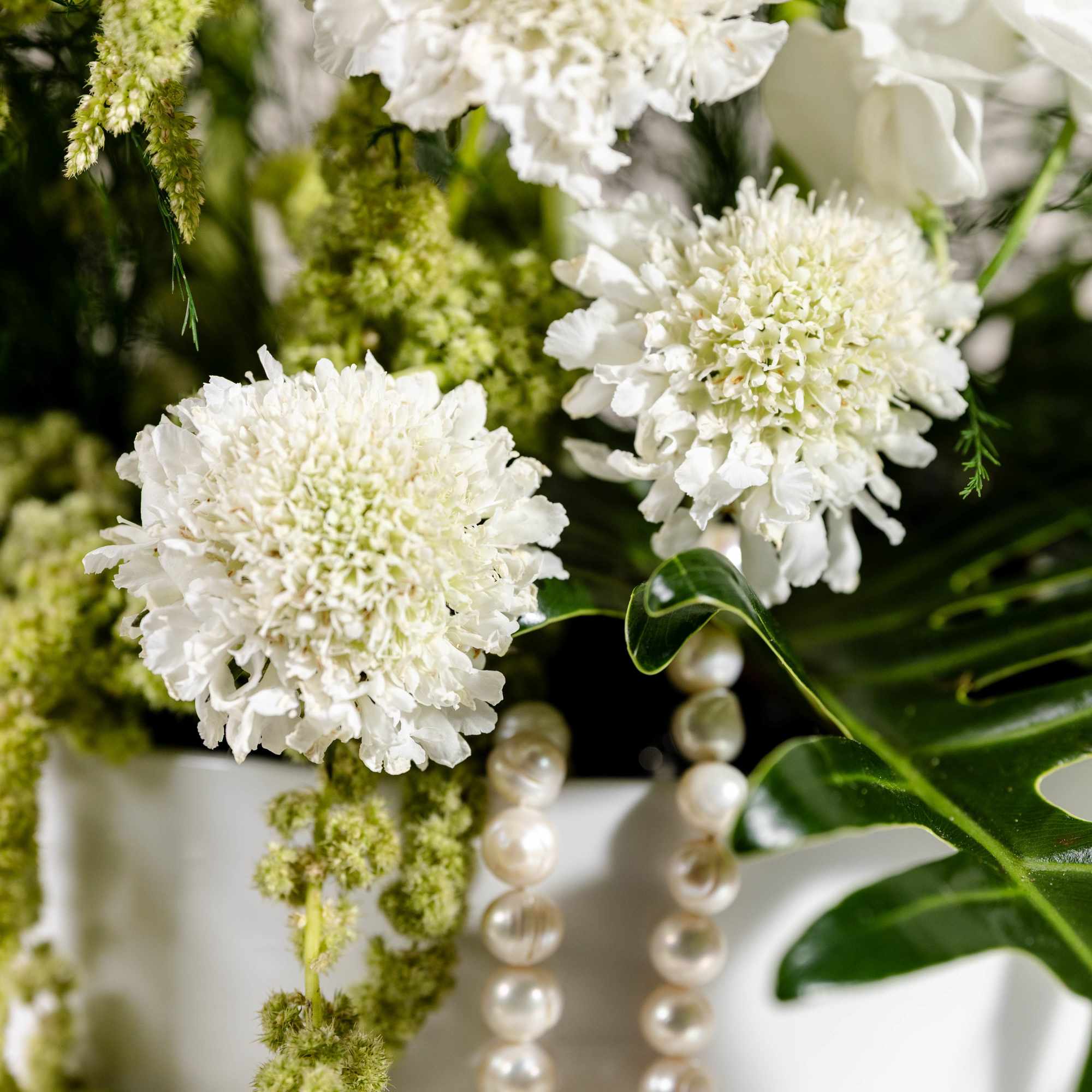 White flowers with green filler and a pearl necklace in a vase