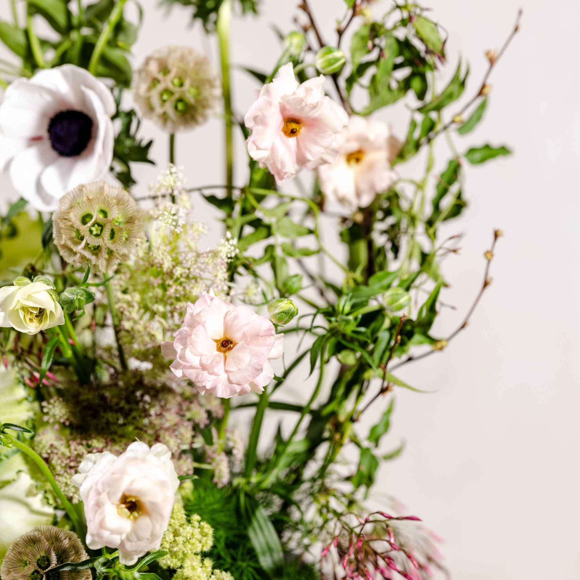 Tall floral arrangement with pale pink blooms and green accents in a vase
