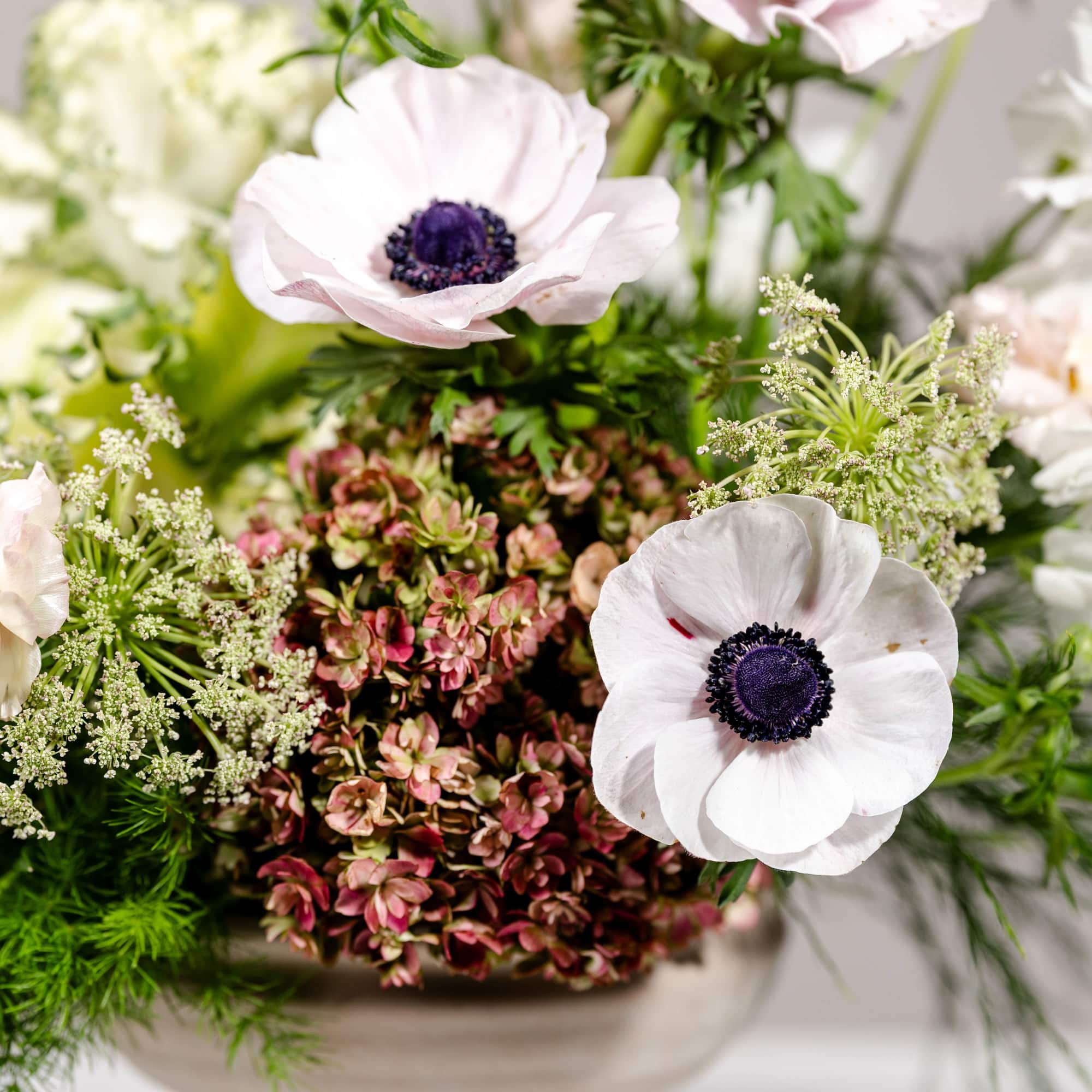 White anemones in a beige pedestal vase with green filler