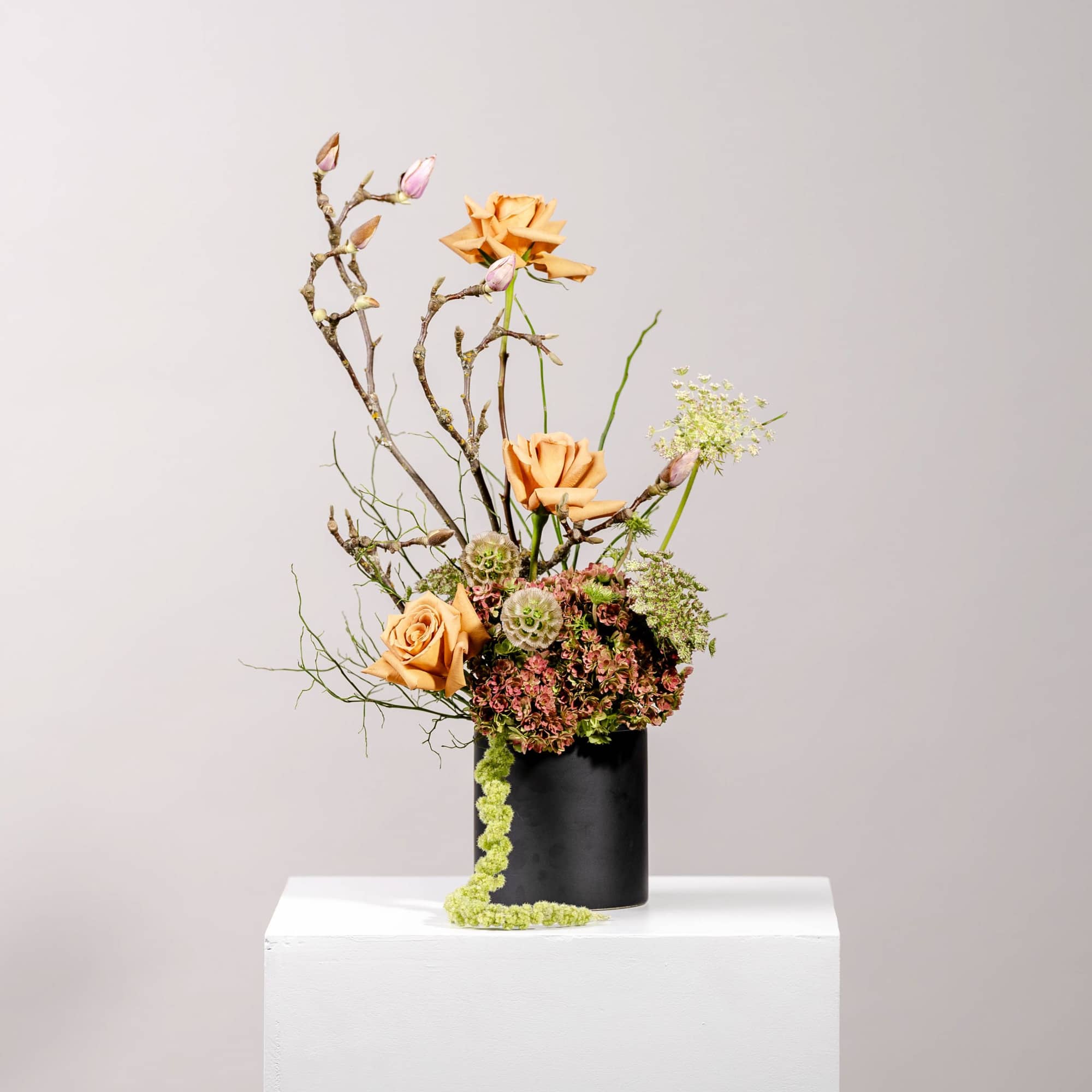 Tall floral arrangement with peach roses in a black vase