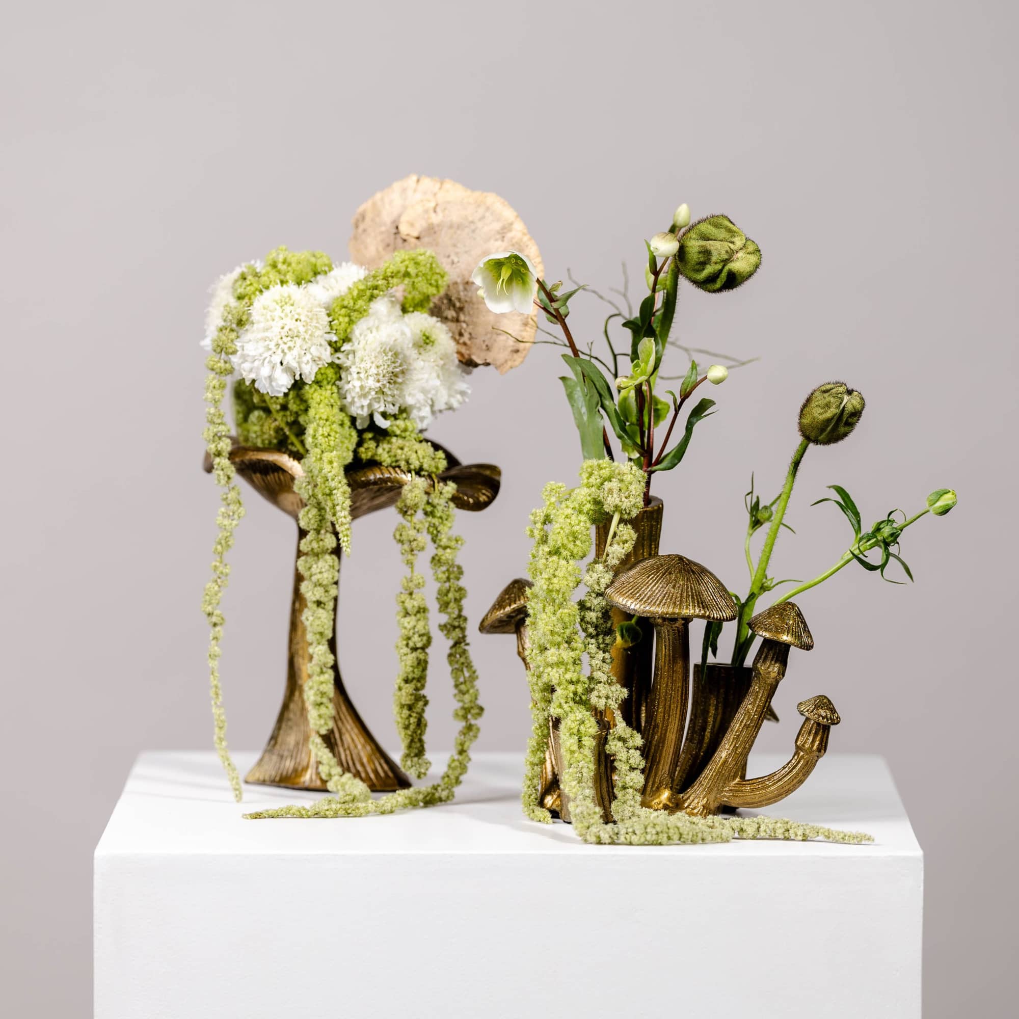 Two floral sculptures with white and green blooms in gold mushroom-shaped holders