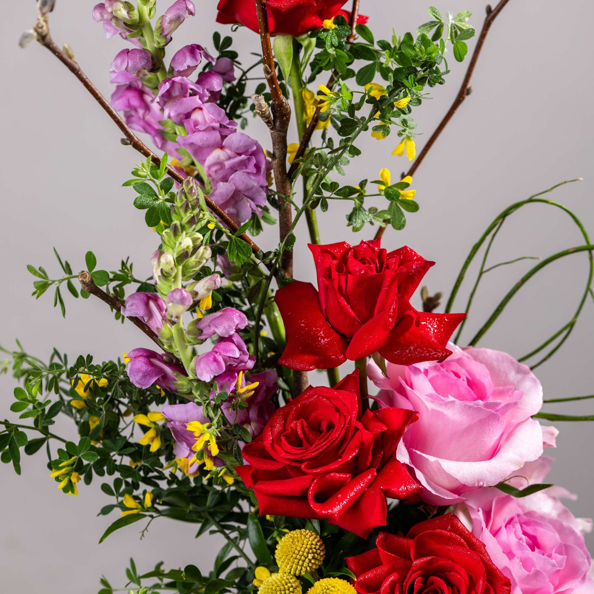Bouquet of red and pink roses with purple snapdragons in a glass vase