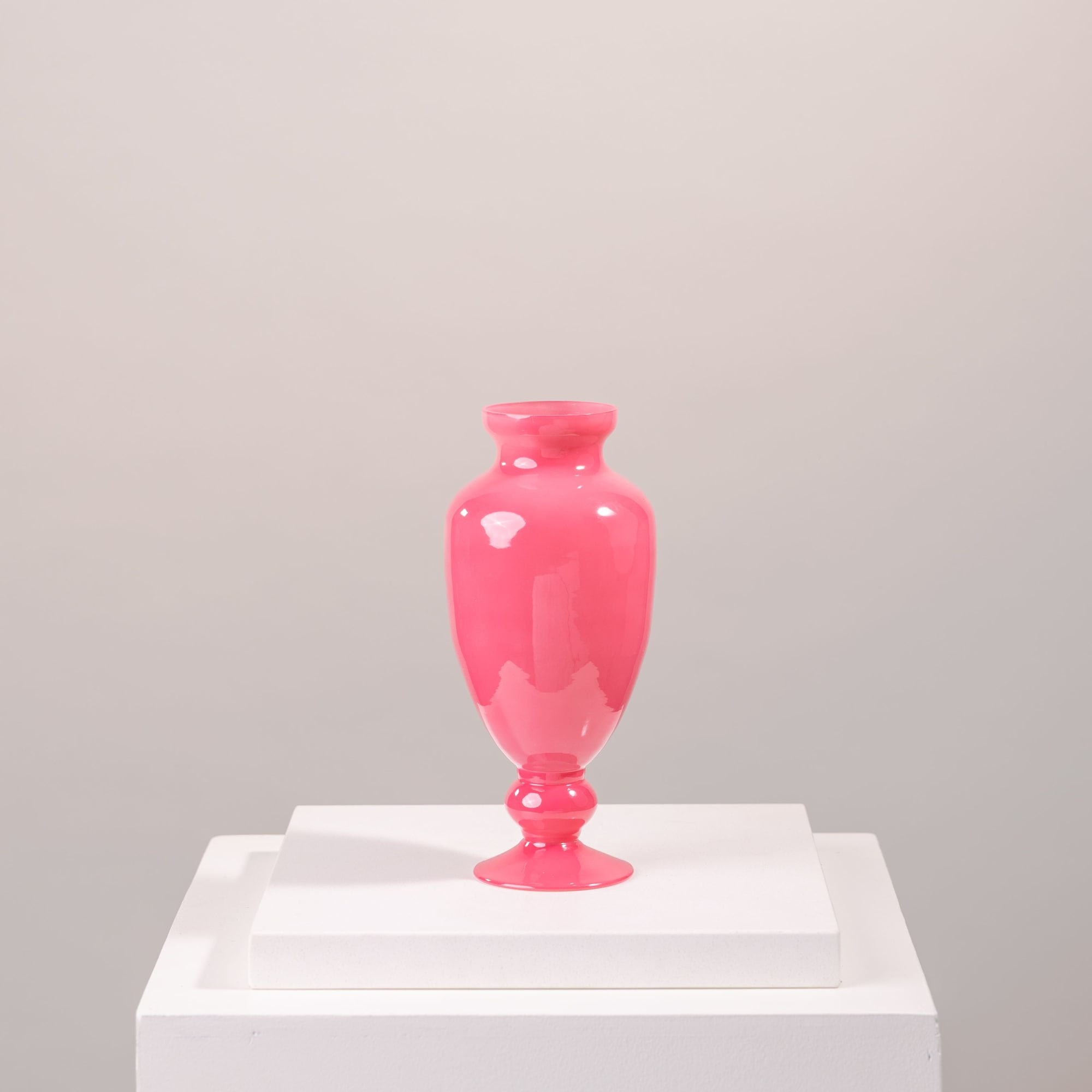 Bright pink glass vase on a white pedestal