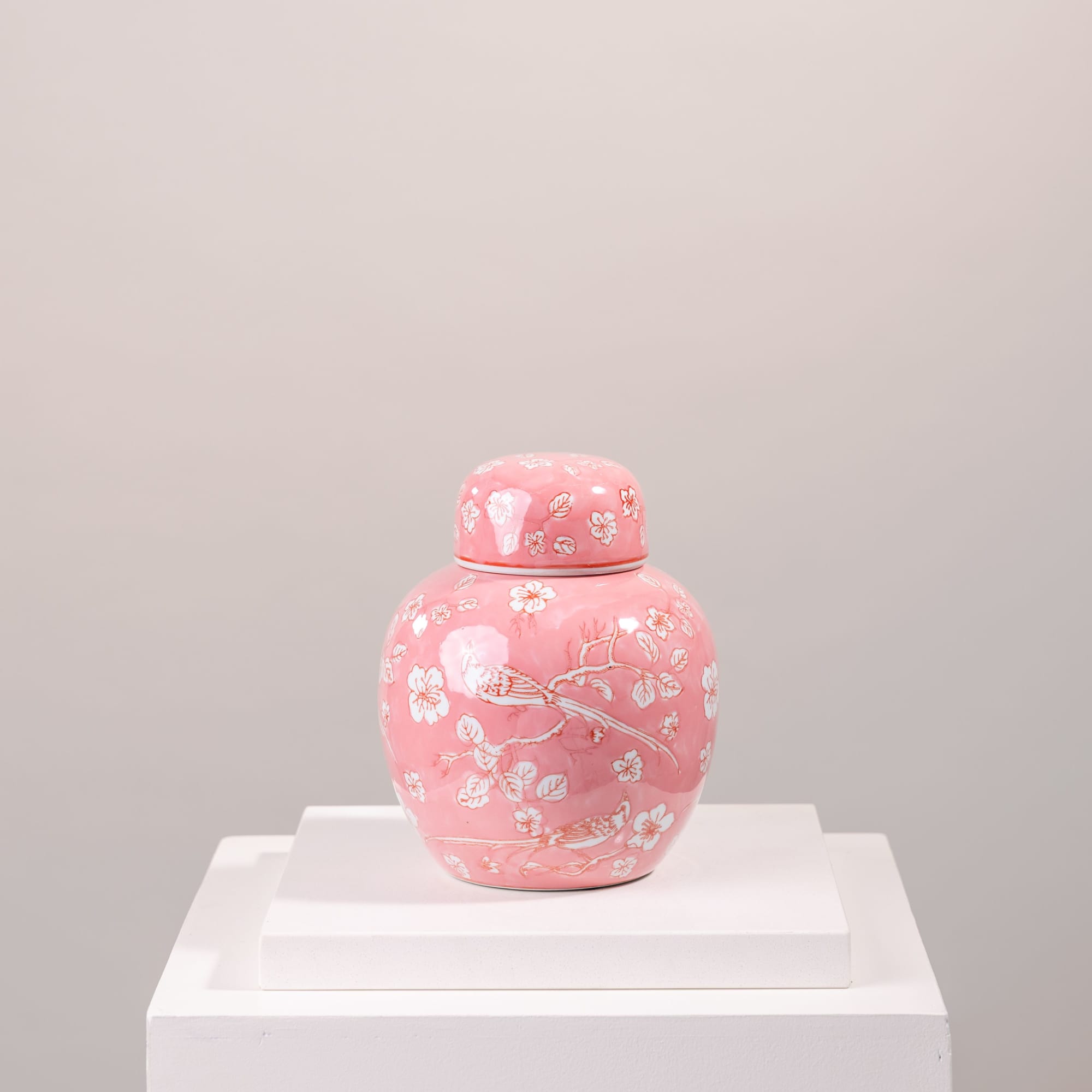Pink ceramic jar with floral and bird pattern on a white pedestal