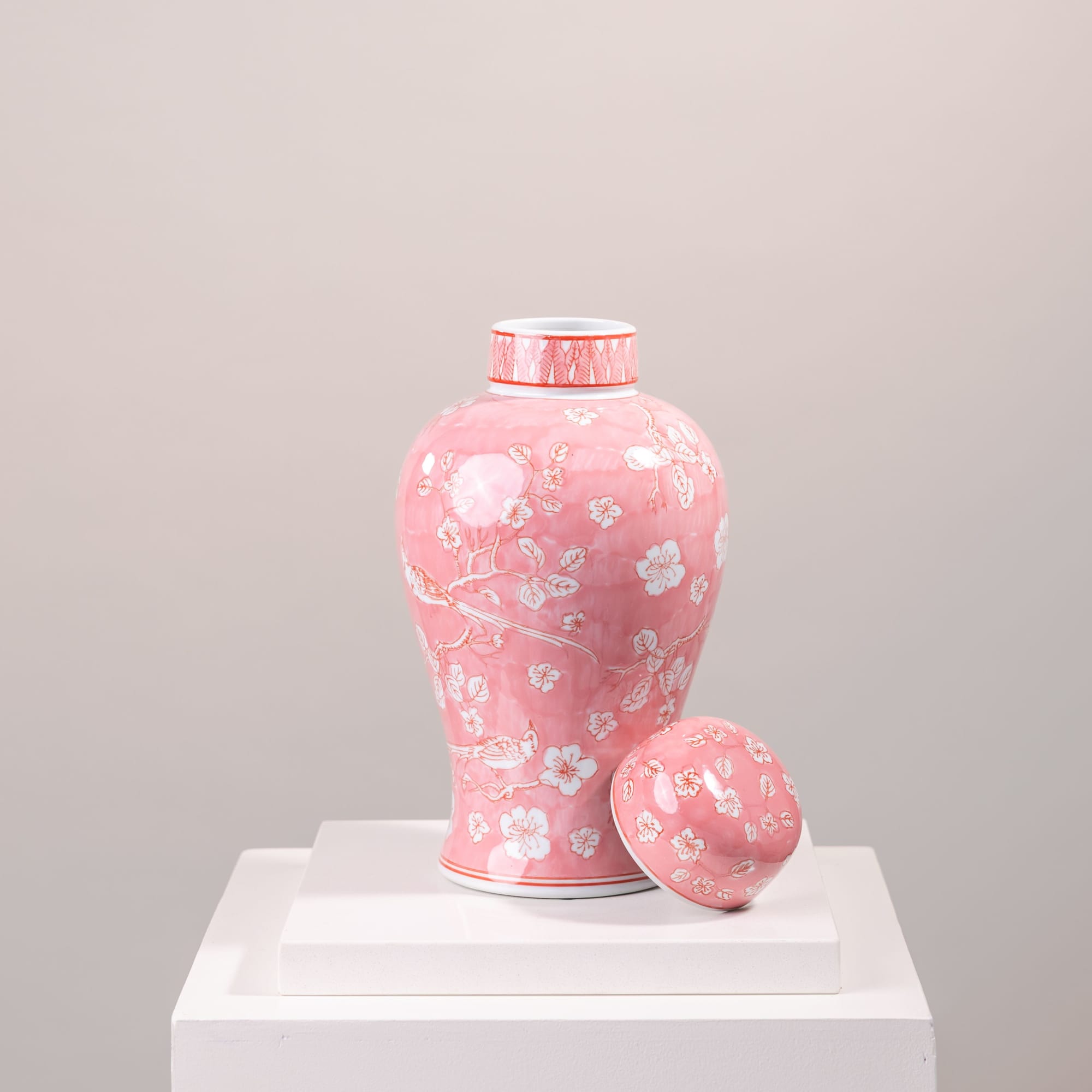 Pink floral ceramic vase with a matching lid on a white pedestal