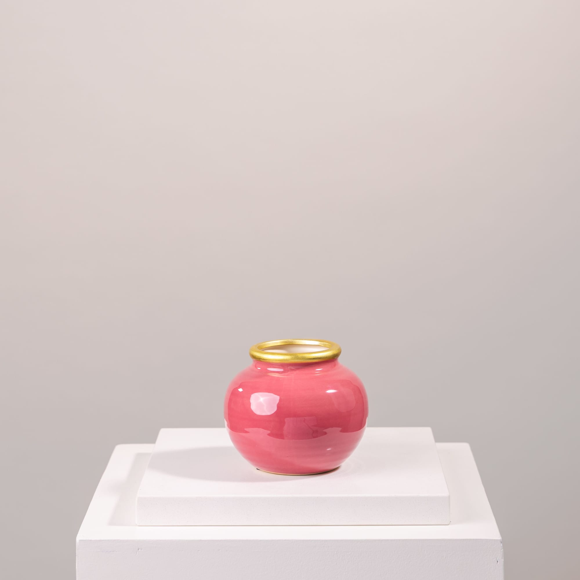Pink ceramic vase with a gold rim on a white pedestal
