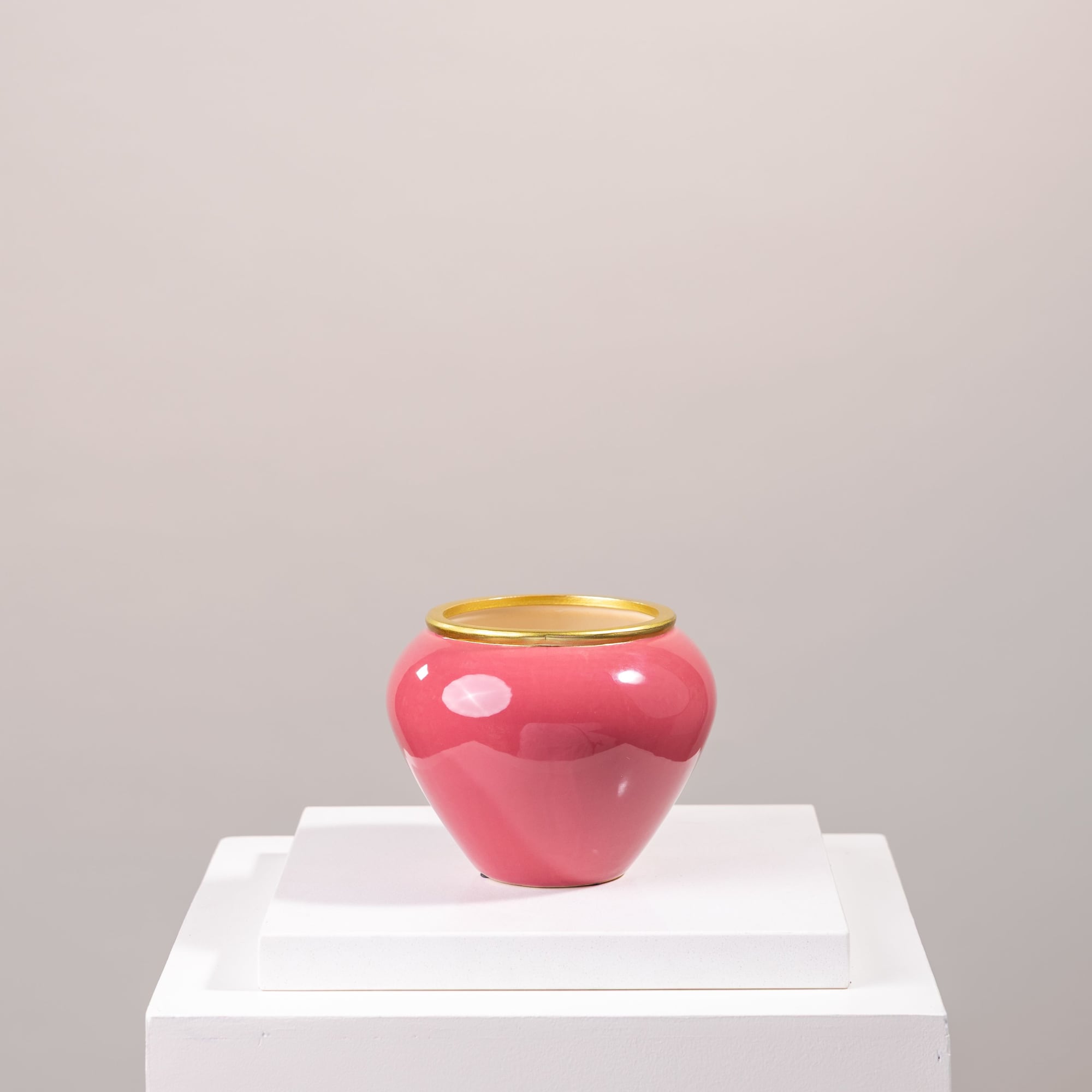 Pink ceramic vase with a gold rim on a white pedestal
