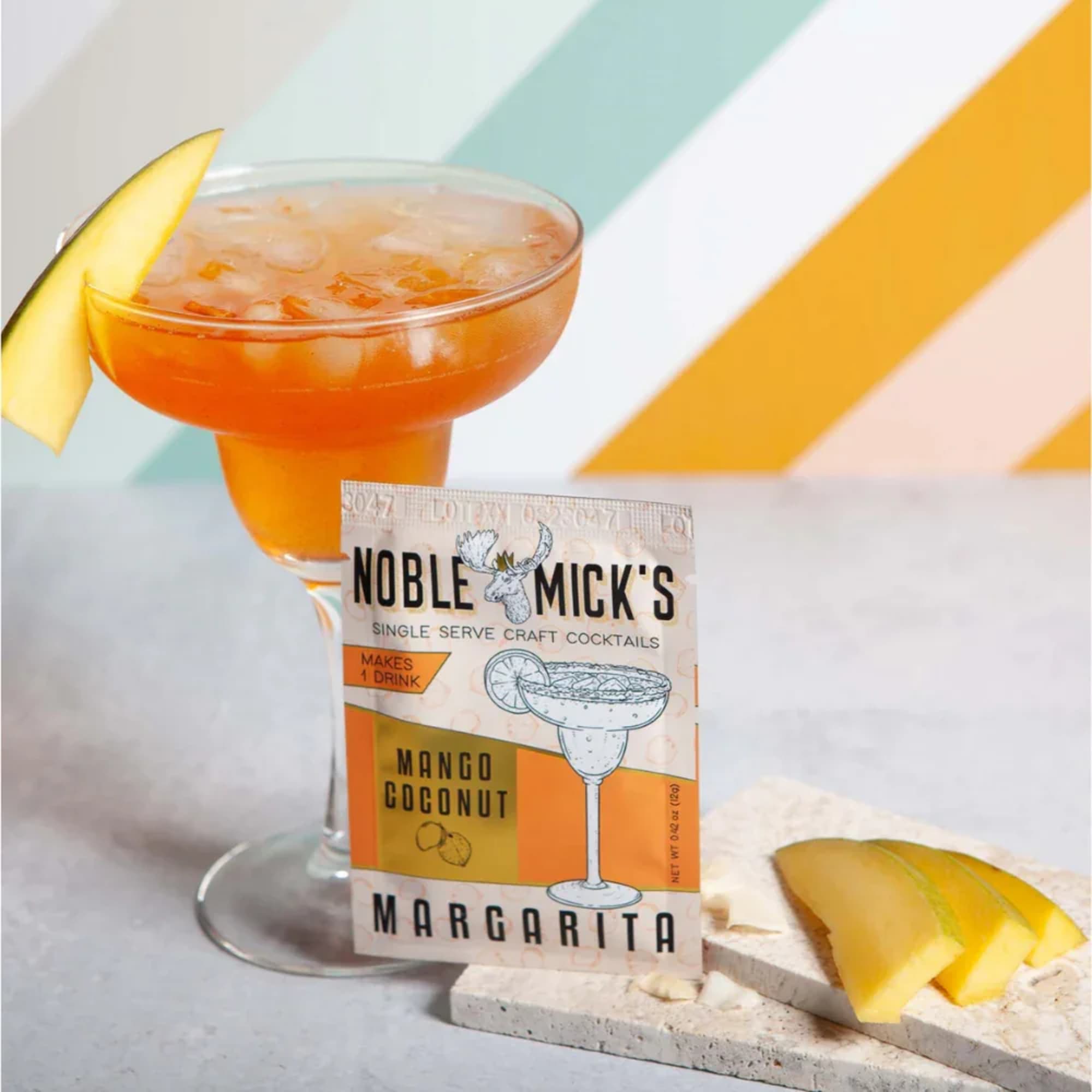Mango coconut margarita in a stemmed glass with mango garnish and a cocktail mix packet