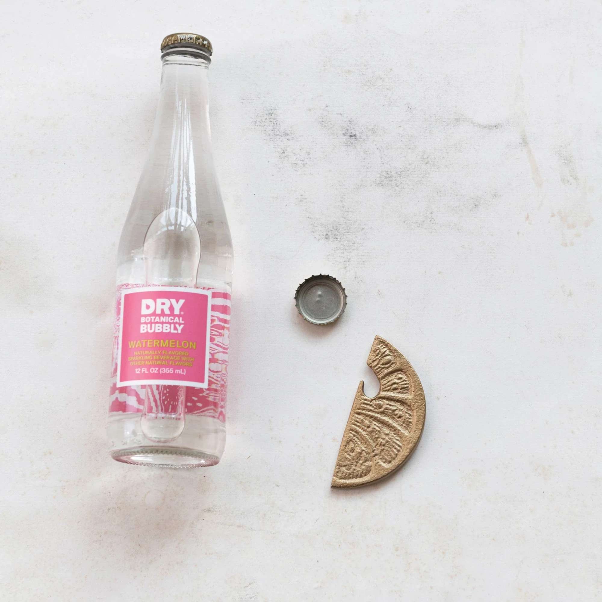 Clear bottle of watermelon sparkling drink with cap and a gold decorative piece