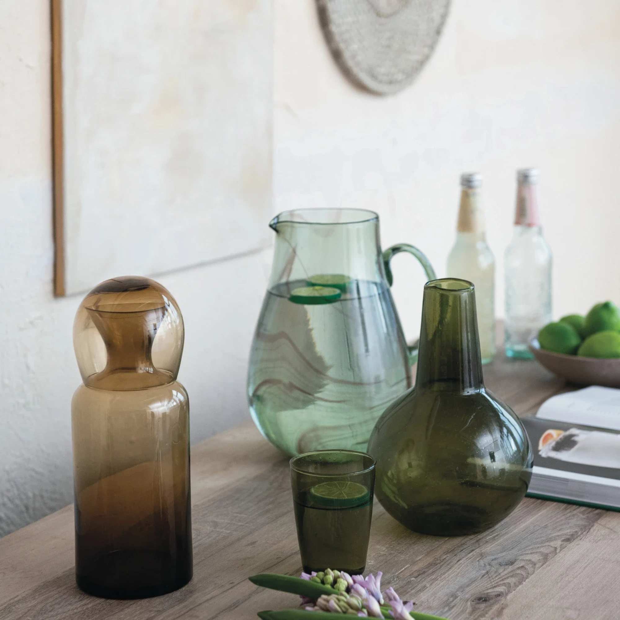 Glass bottles and pitchers on a table with a small flower cluster in front
