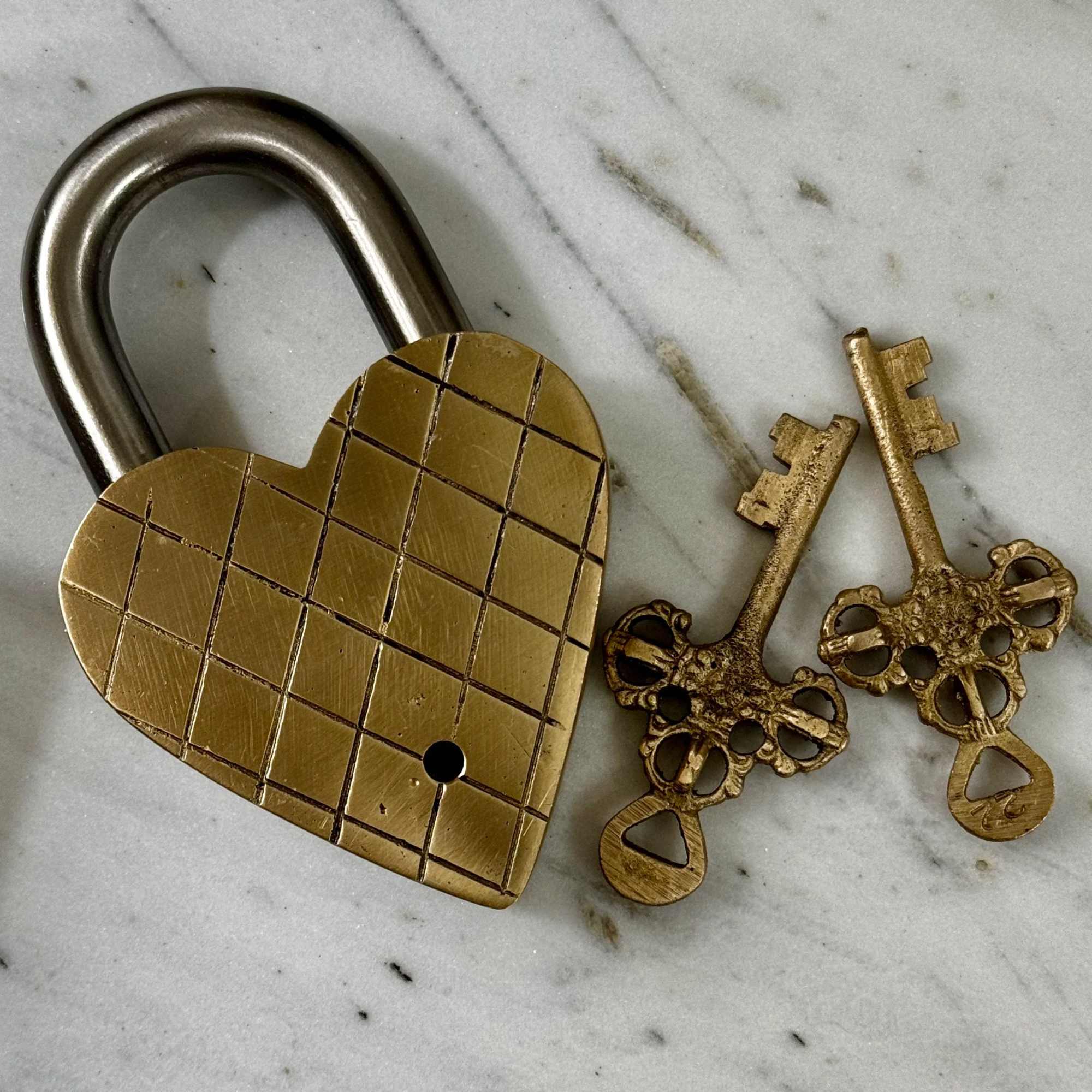 Brass heart-shaped padlock with three ornate keys on a marble surface
