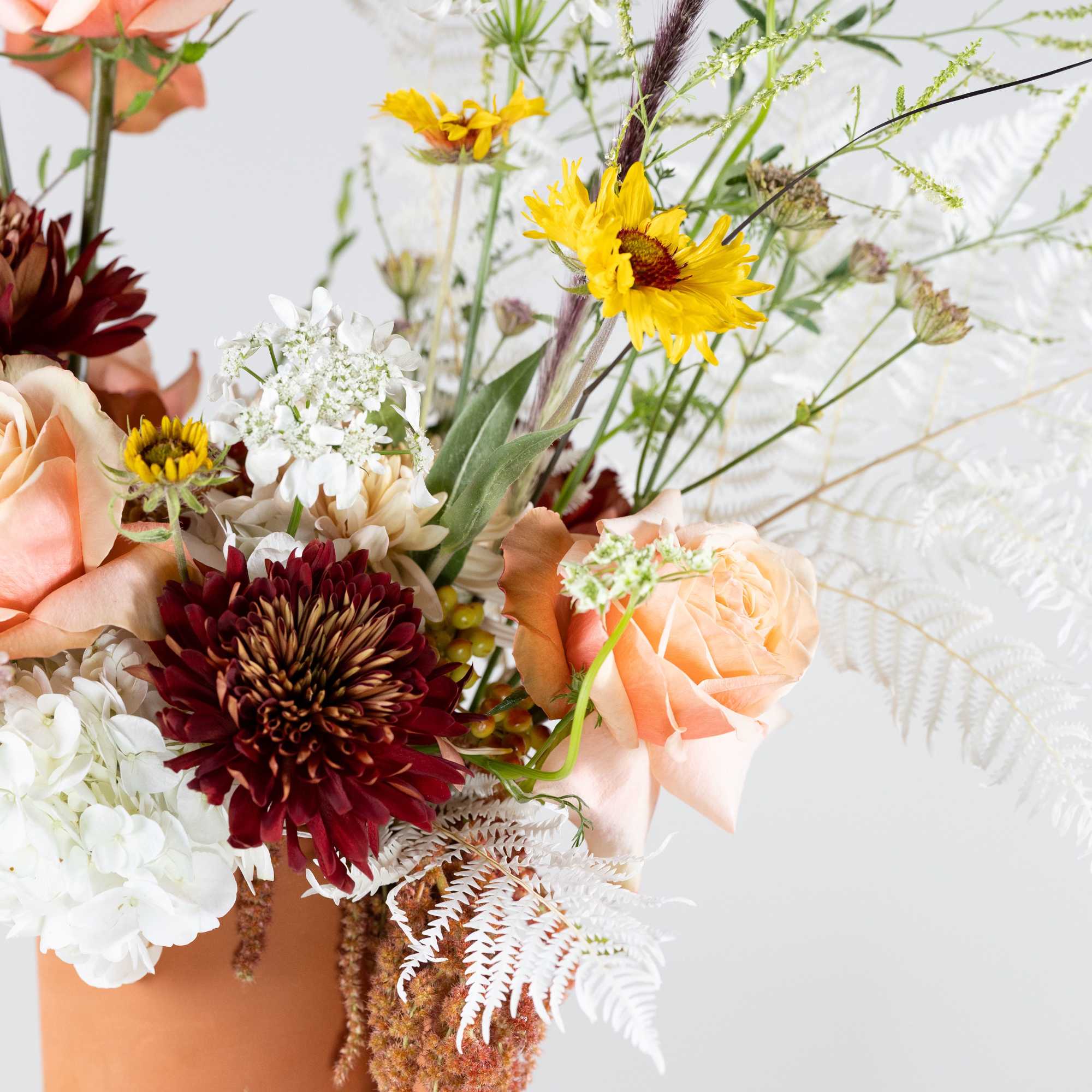 Mixed bouquet in a terracotta vase with peach, white, and burgundy flowers