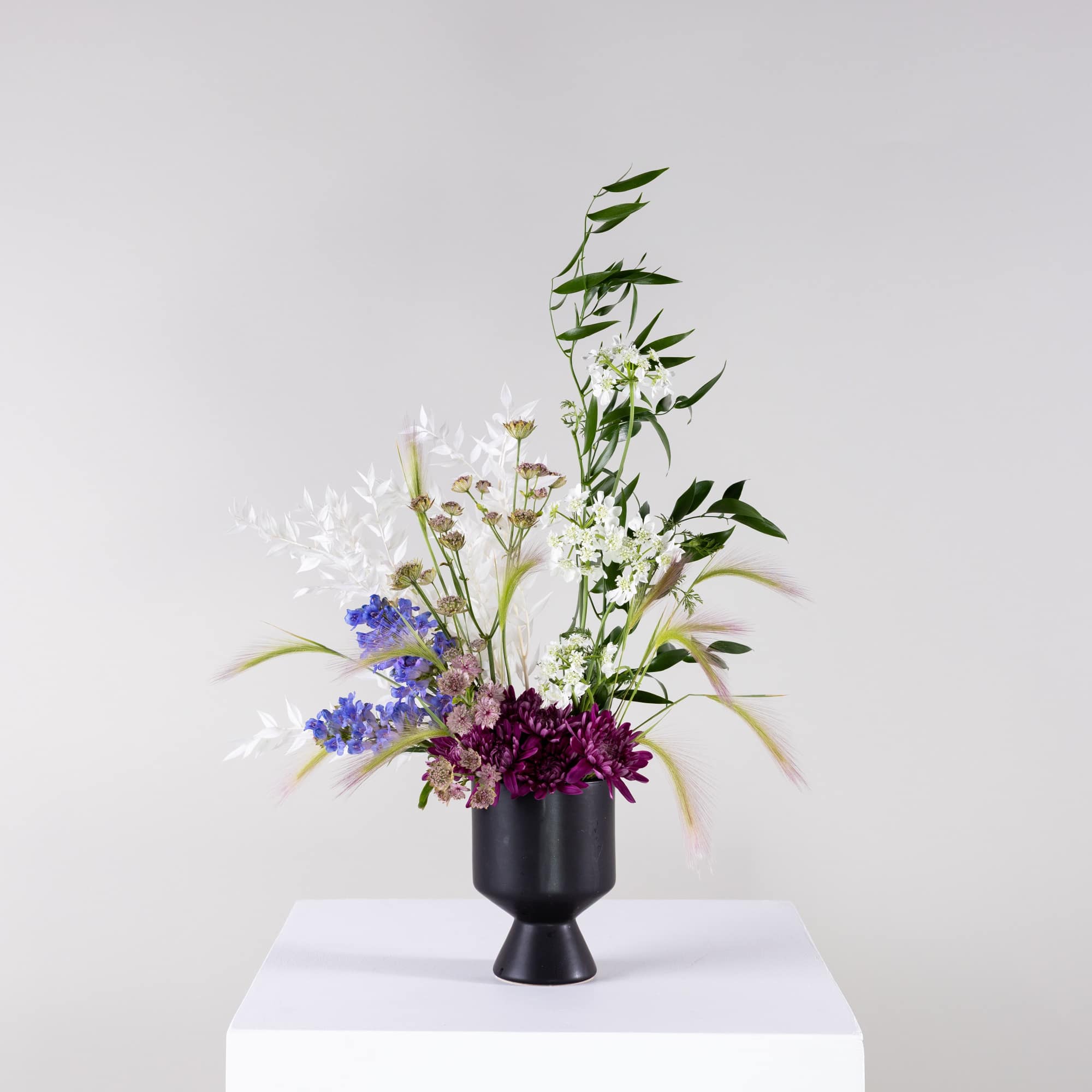 Tall mixed bouquet in a black pedestal vase with purple, blue, and white flowers