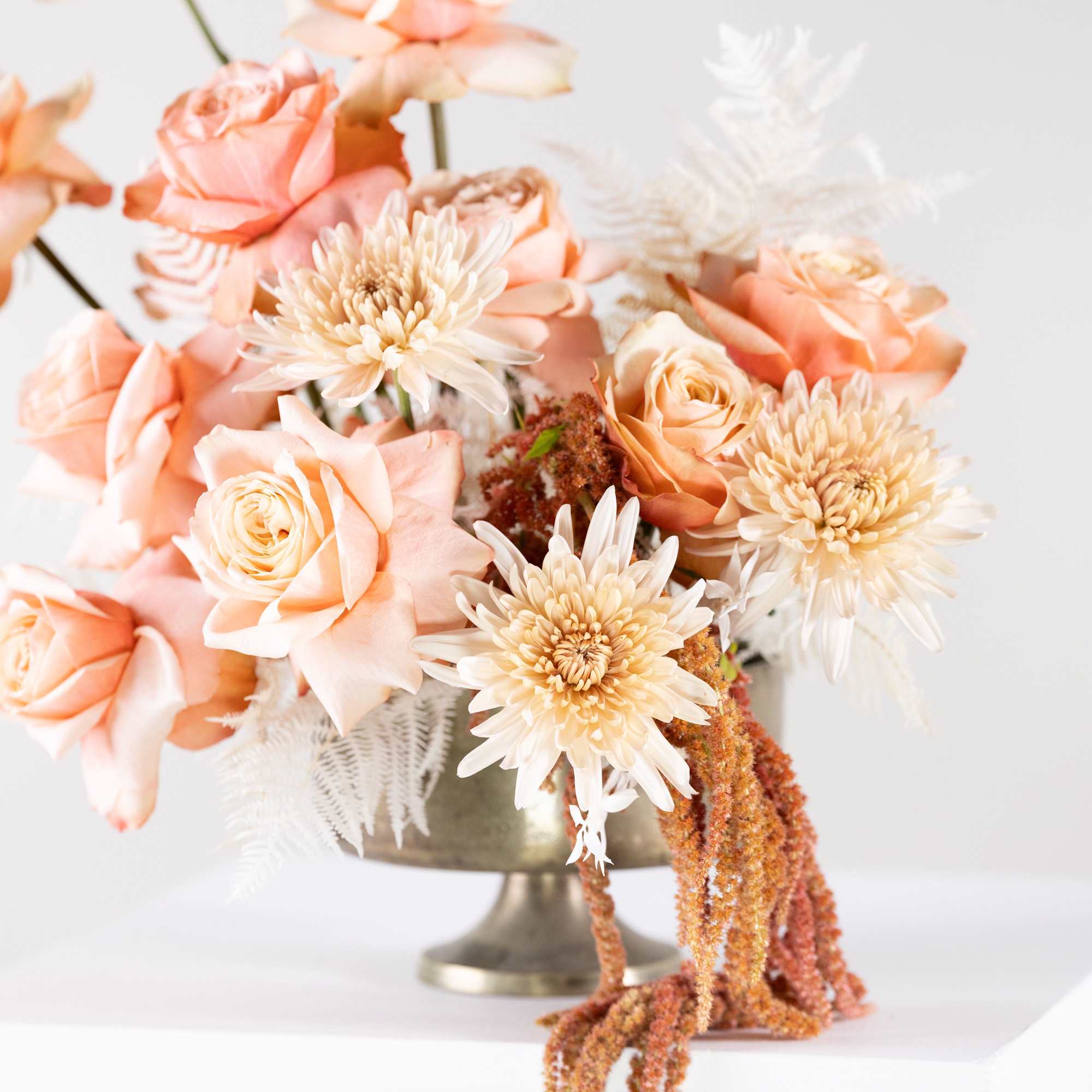Peach roses and cream chrysanthemums in a metal pedestal vase